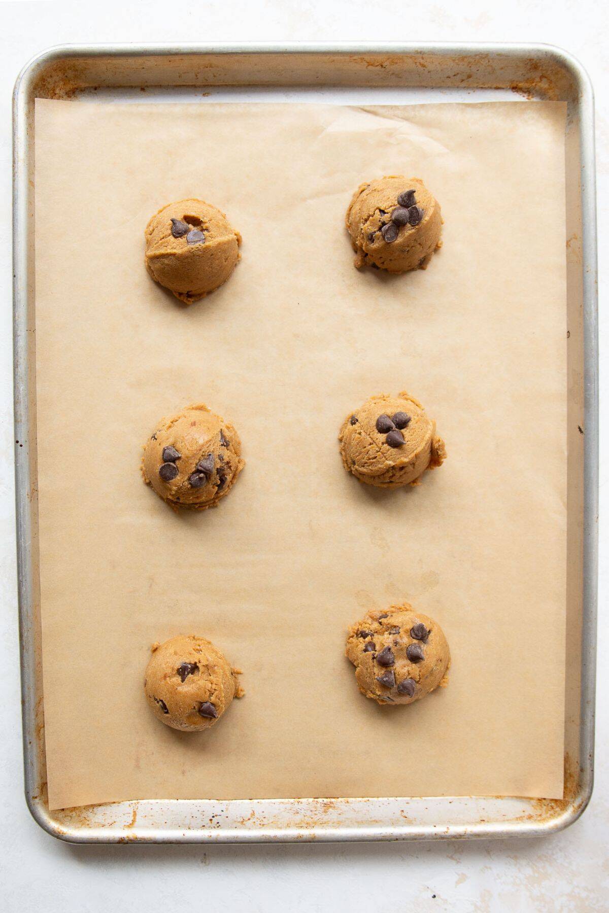 Protein chocolate chip cookie dough balls on a parchment-lined baking sheet with extra chocolate chips pressed on top.
