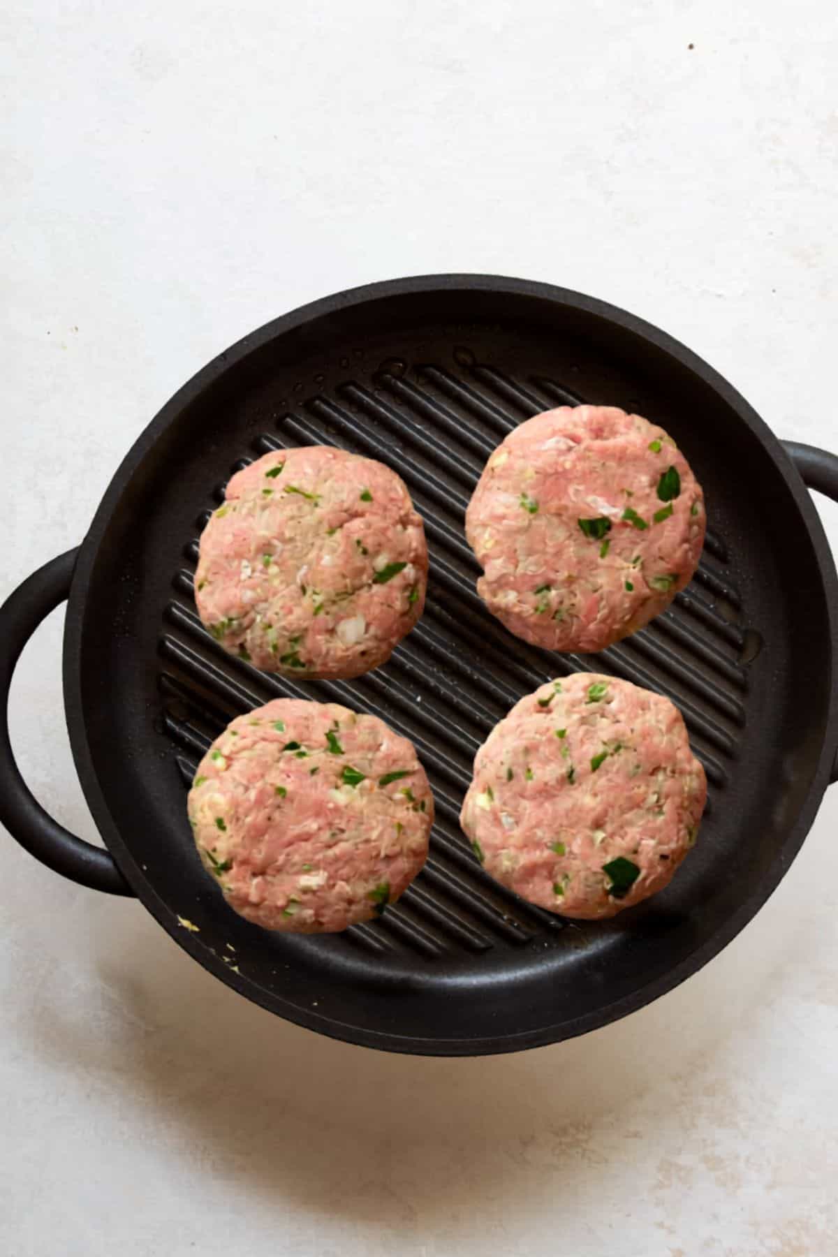 Turkey burger patties cooking on a hot grill pan with grill marks.