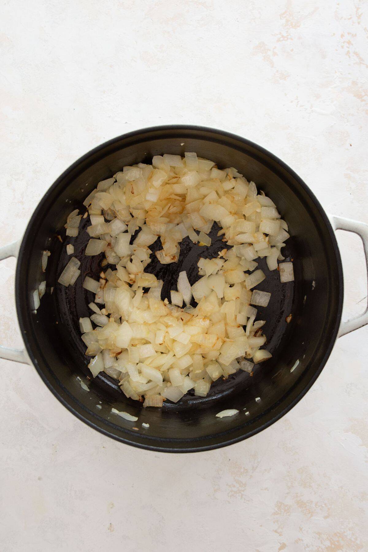 Diced onions sautéing in olive oil in a Dutch oven for pasta bake.