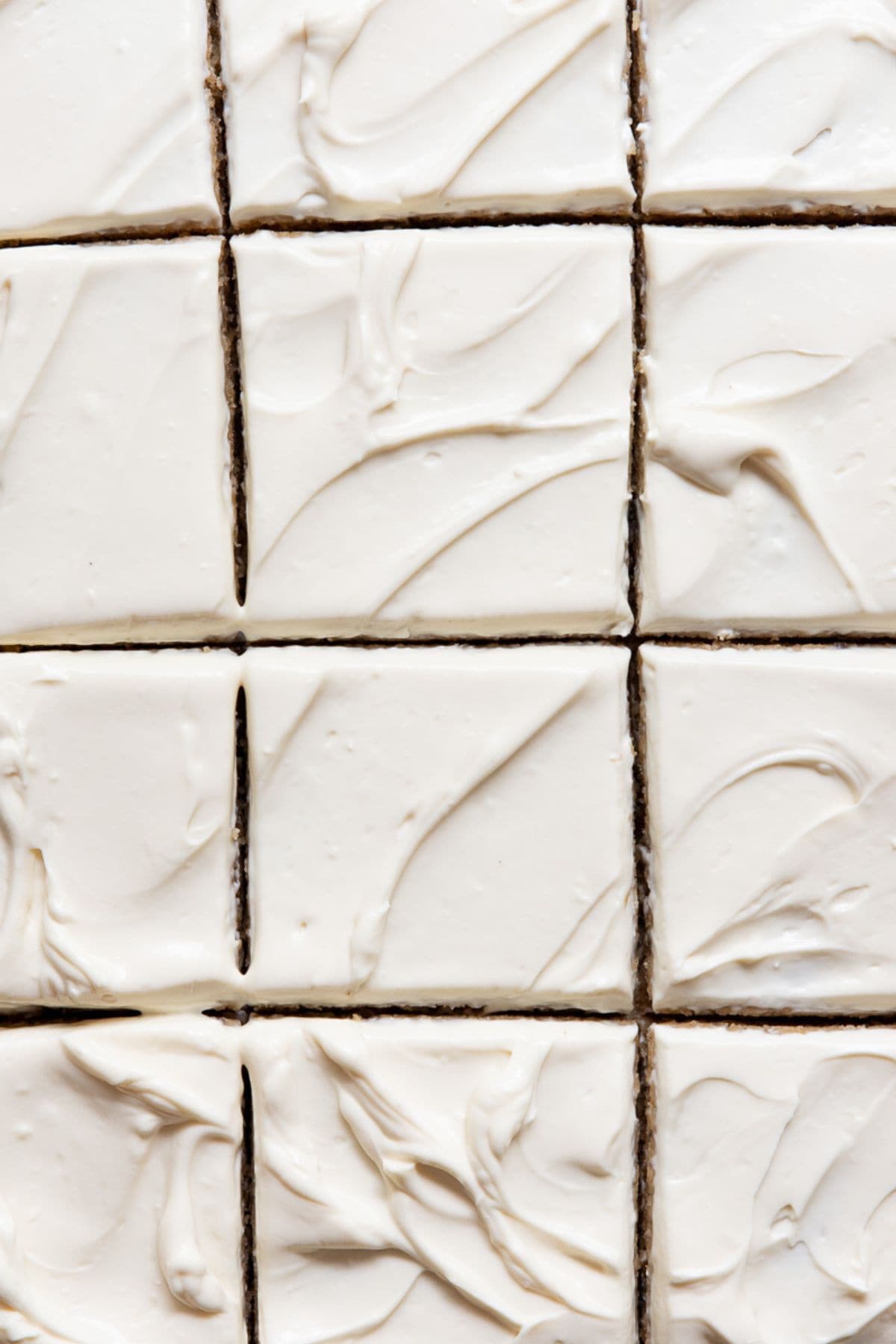 Healthy cream cheese frosting spread across a sheet cake cut intro squares.