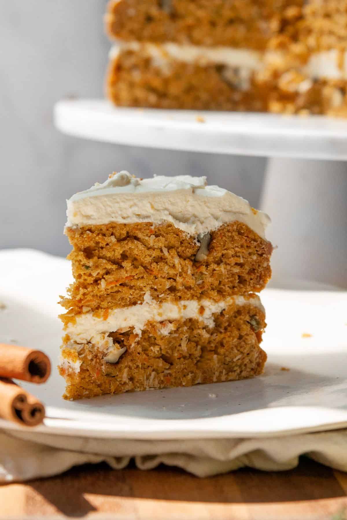 A slice of pumpkin carrot cake topped with healthy cream cheese frosting on a white plate.