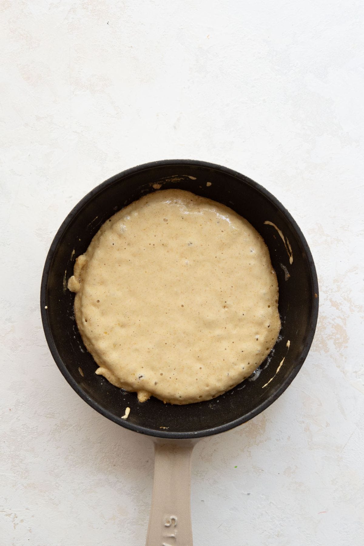 Oat flour pancake batter cooking in a buttered skillet before flipping.