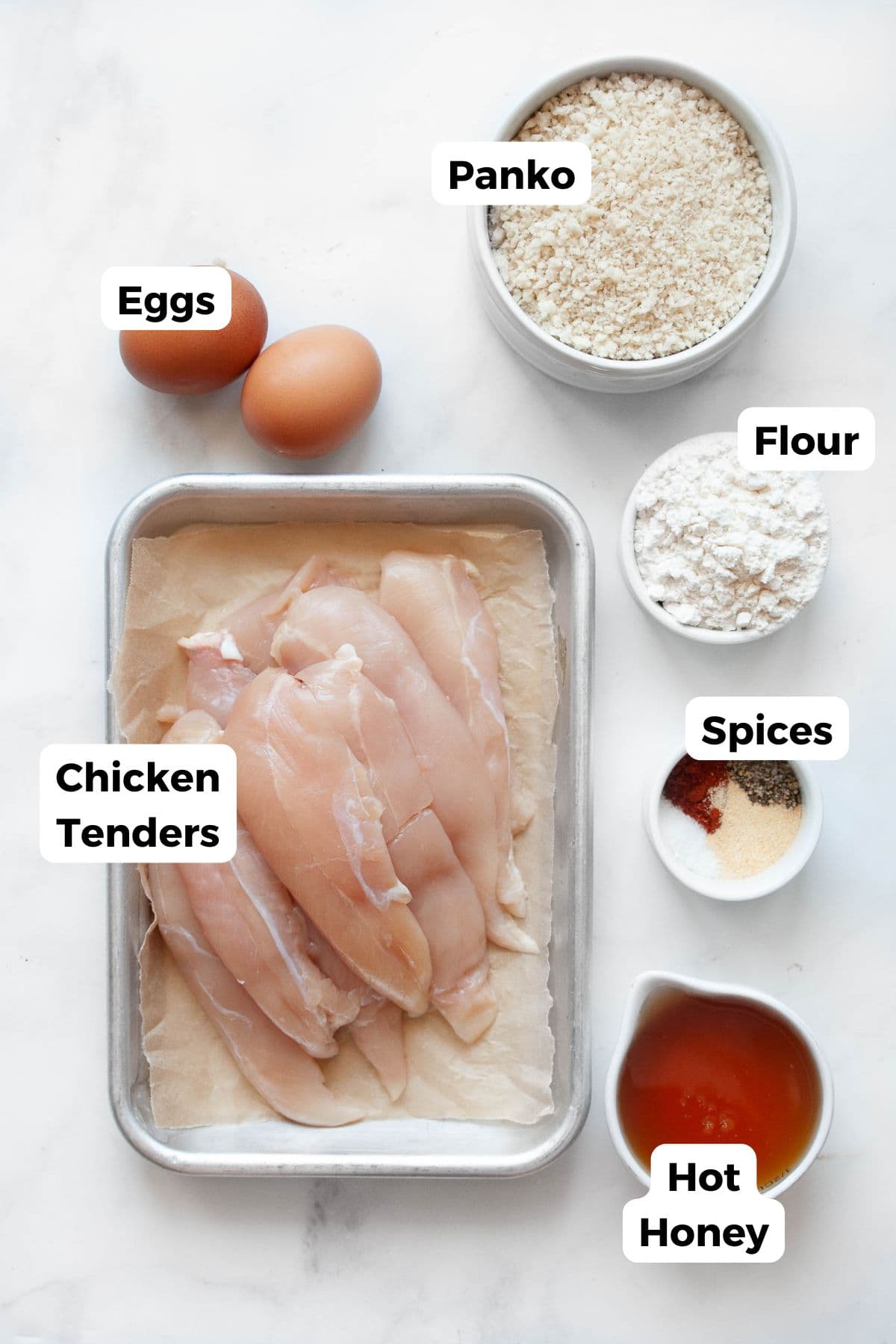 All ingredients for hot honey chicken tenders displayed in labeled bowls, including chicken tenders, flour, eggs, panko breadcrumbs, paprika, garlic powder, salt, pepper, and hot honey sauce.