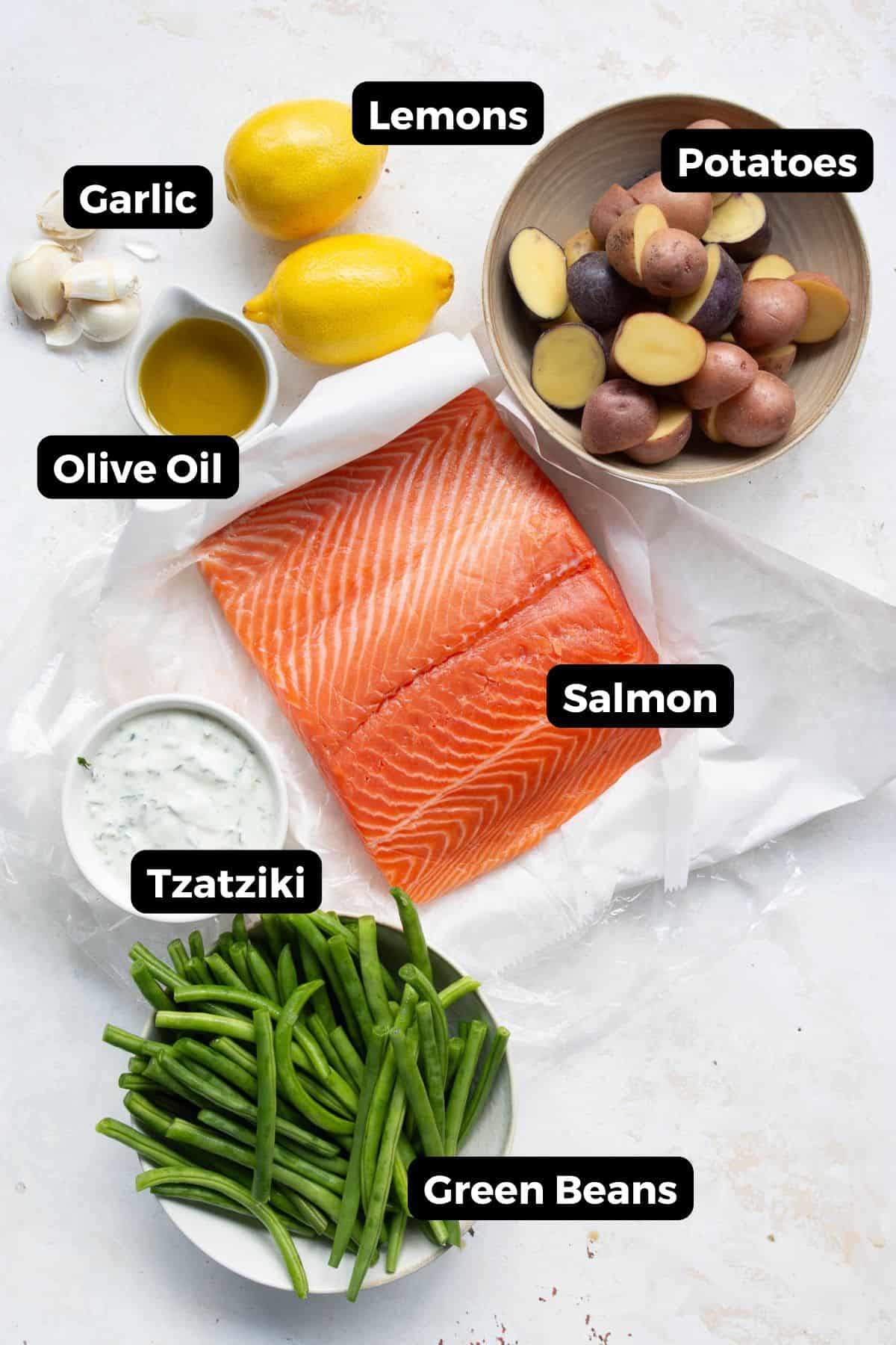 Ingredients for sheet pan salmon and veggies including salmon, potatoes, green beans, lemon, garlic, olive oil, tzatziki, and dill.