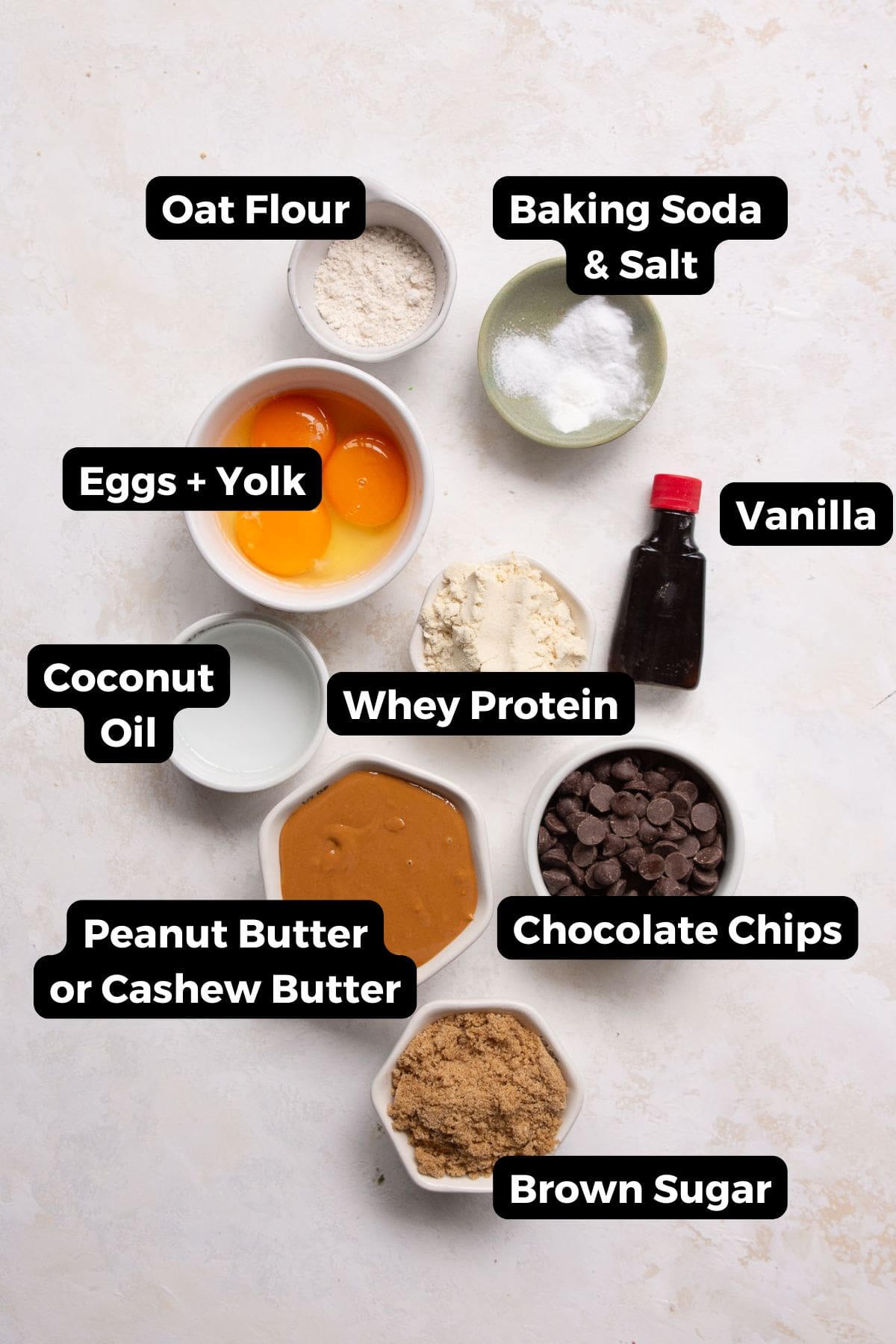 All ingredients for protein chocolate chip cookies including peanut butter, eggs, whey protein powder, oat flour, and chocolate chips.
