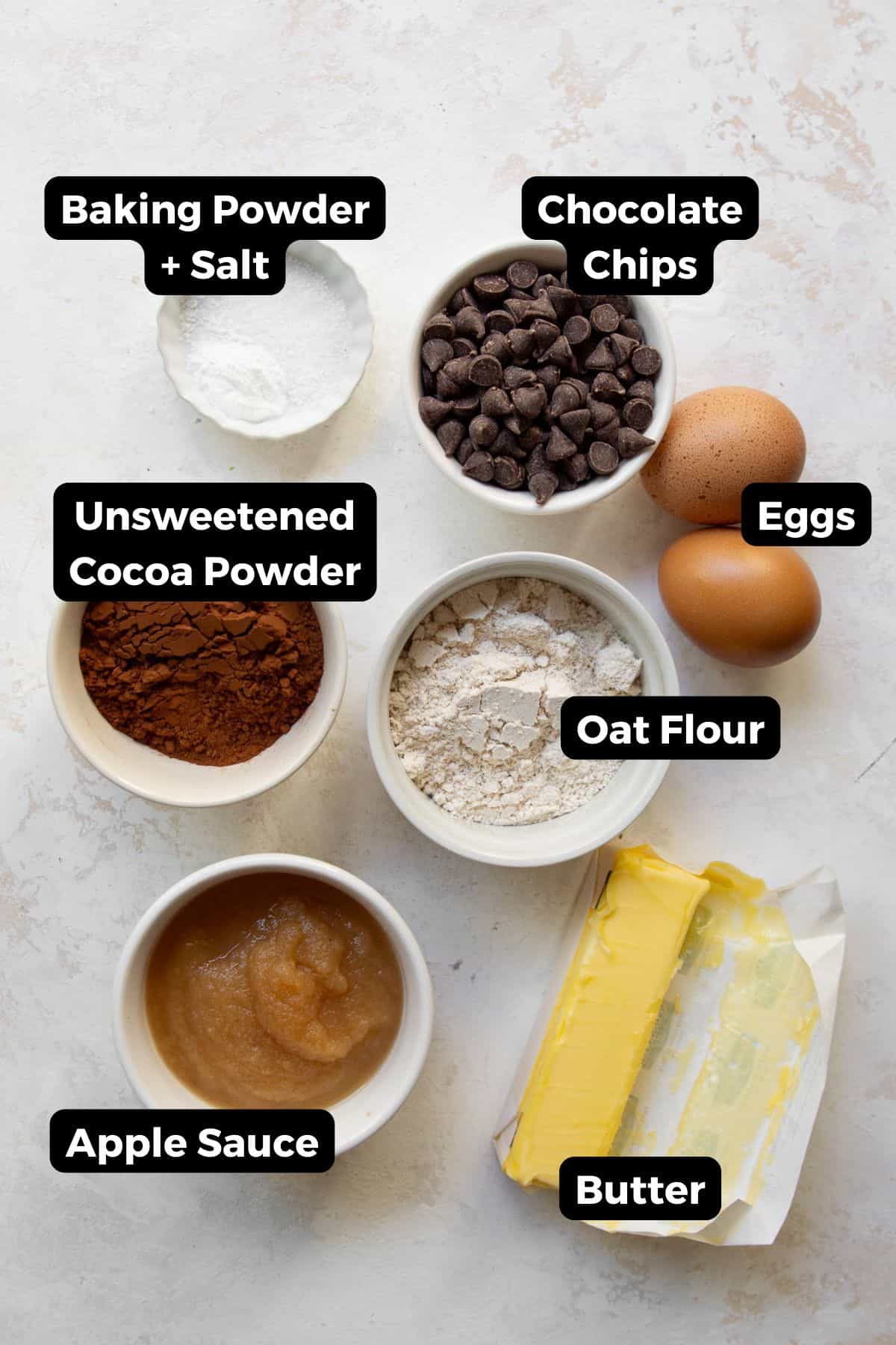 Ingredients for oat flour brownies including oat flour cocoa powder chocolate chips eggs applesauce butter baking powder and salt.