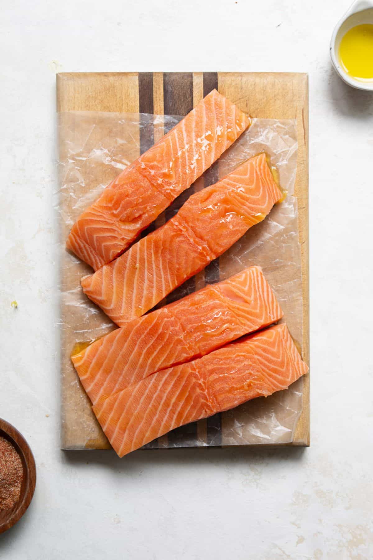 Skin-on salmon fillets on parchment paper drizzled with olive oil.