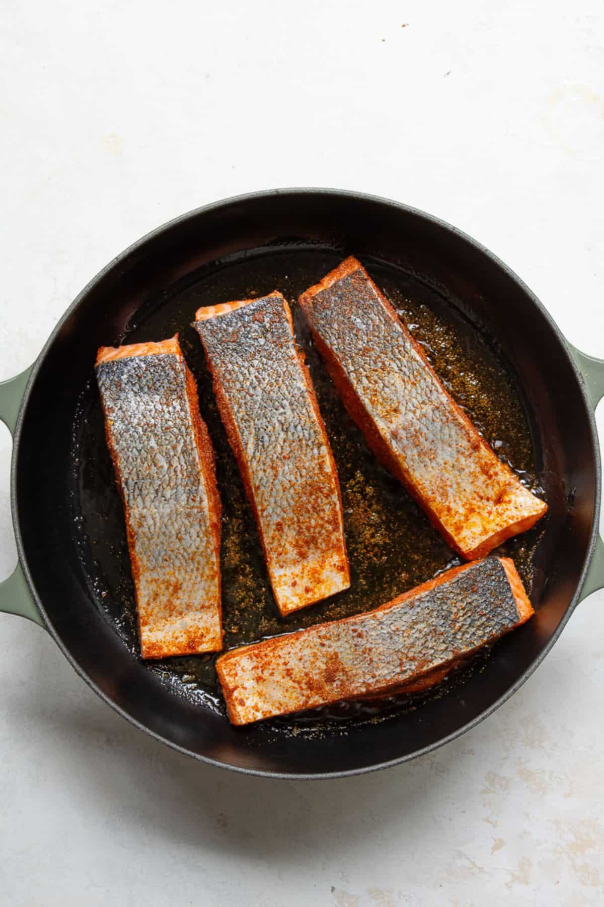 Cajun-seasoned salmon fillets searing skin-side up in a cast iron skillet.