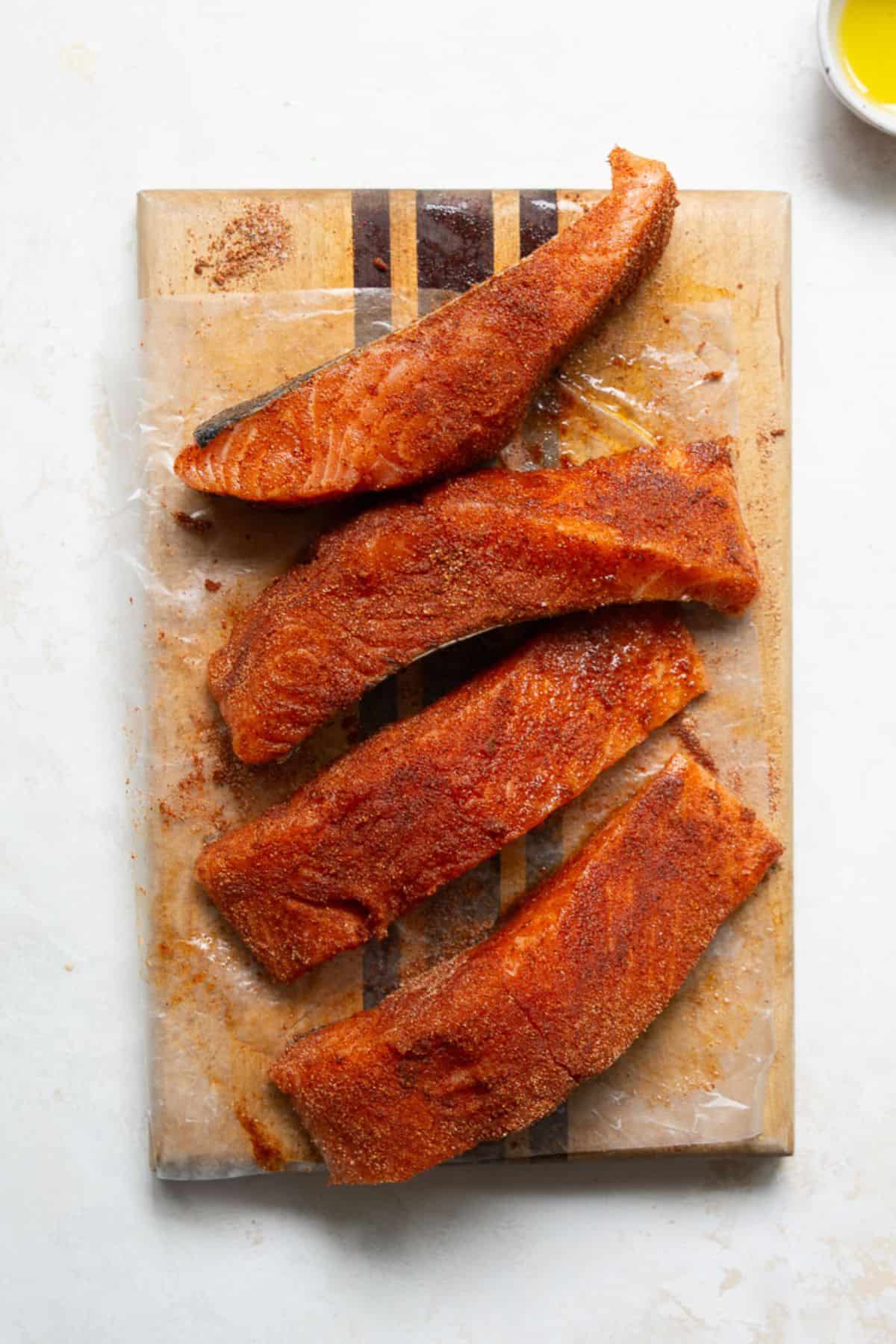 Four salmon fillets coated in Cajun blackening seasoning on a wooden cutting board, ready to be pan-seared