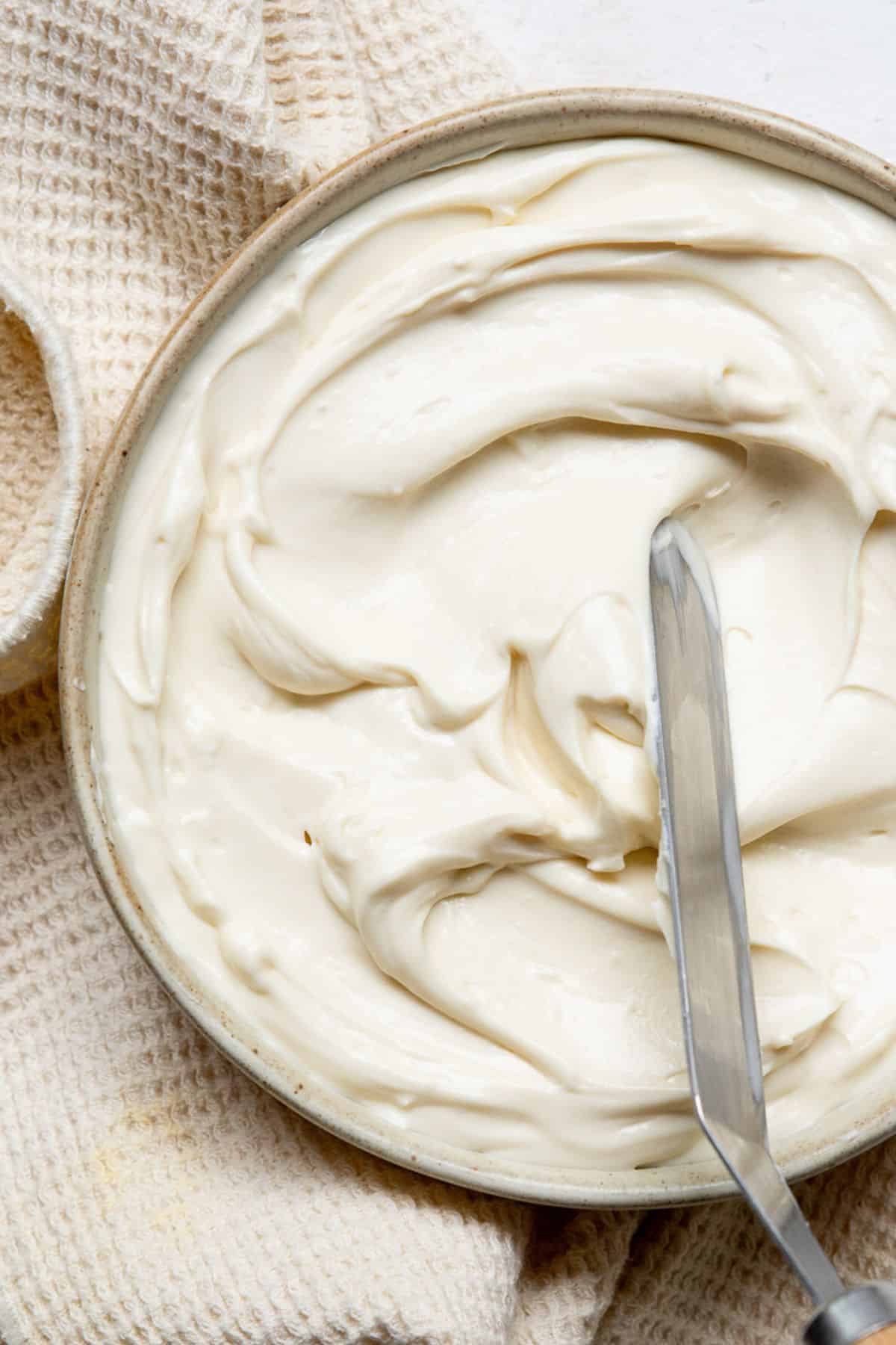 Thick and fluffy healthy cream cheese frosting swirled in a white bowl, ready to spread.