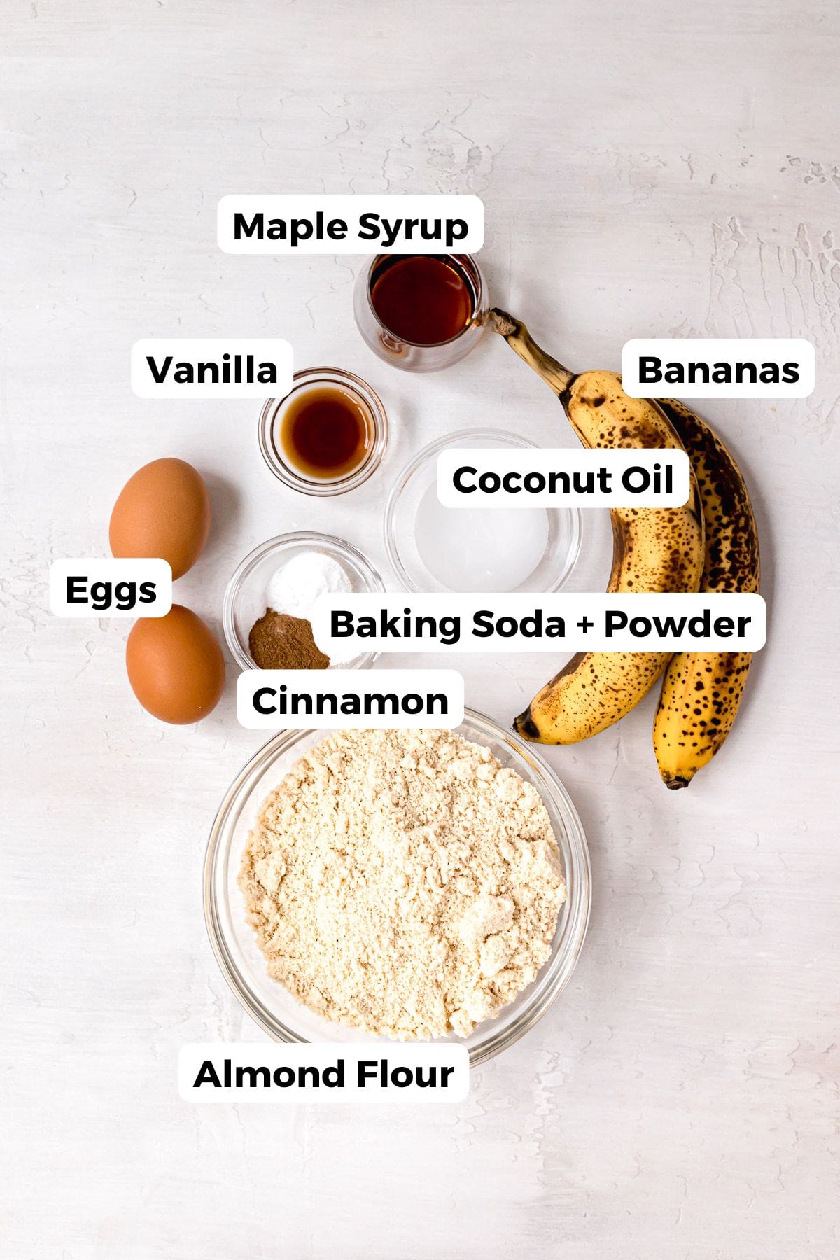 All ingredients in almond flour banana muffins, including: bananas, almond flour, maple syrup, eggs, baking soda, baking powder, vanilla, cinnamon, and coconut oil.