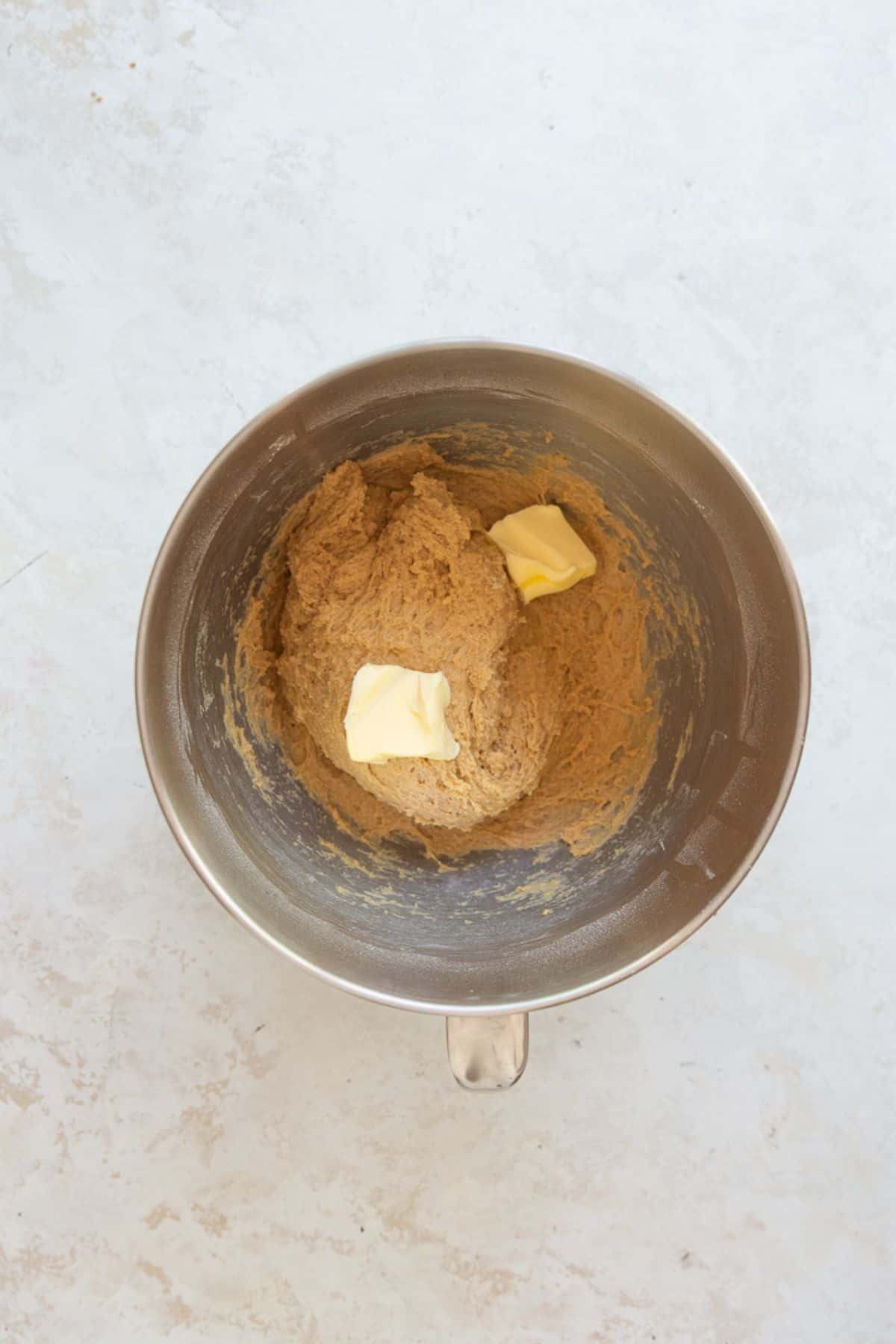 Pieces of softened butter being added to cinnamon roll dough in a stand mixer bowl.