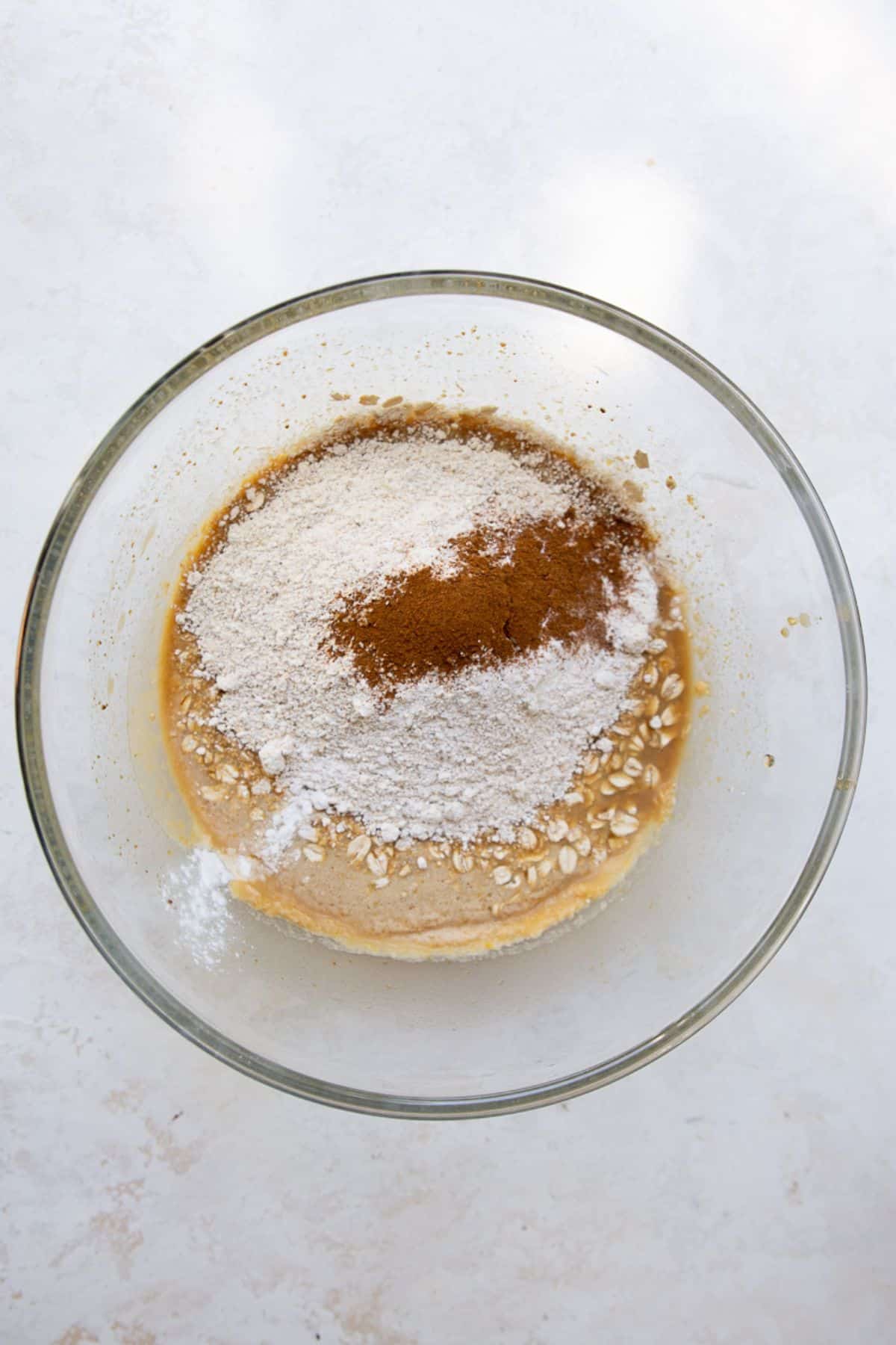 Adding oat flour, cinnamon, and baking powder to the wet batter for healthy chocolate chip oatmeal bars in a glass bowl.