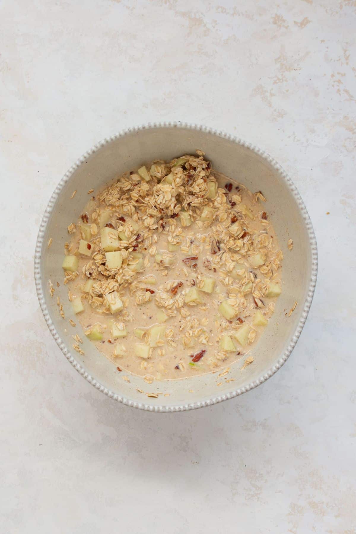 Apple cinnamon baked oatmeal batter with chopped apples and pecans in a mixing bowl.