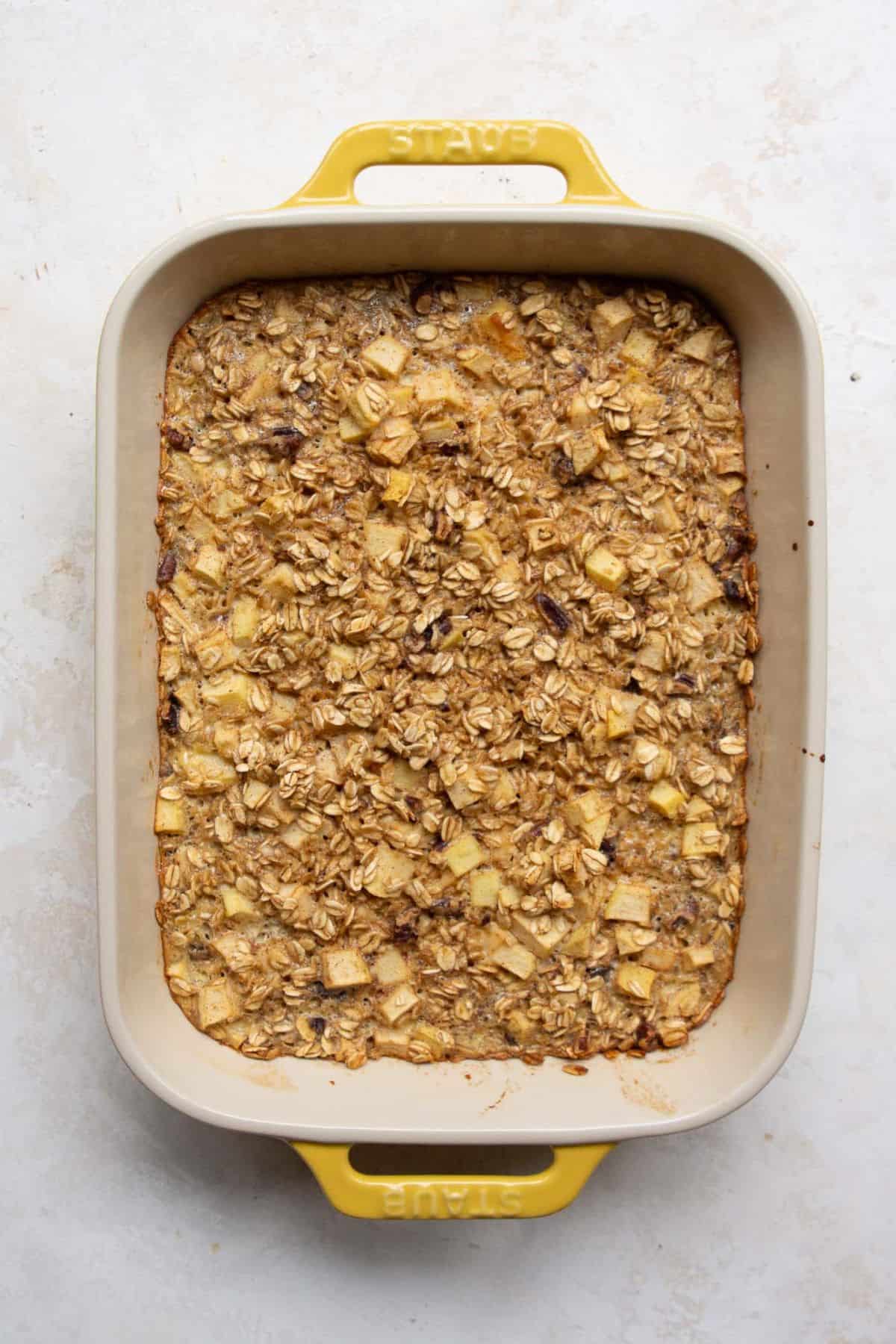 Healthy apple cinnamon baked oatmeal fresh from the oven in a yellow baking dish.