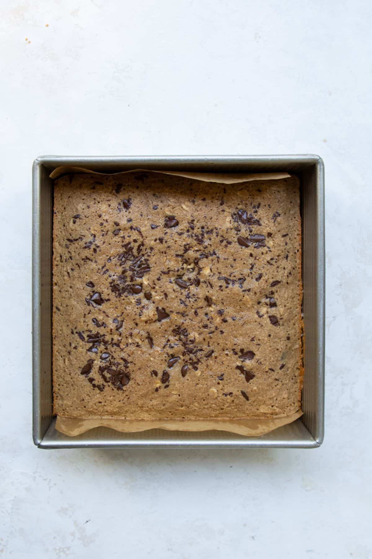 Freshly baked healthy chocolate chip oatmeal bars in a square metal baking pan, topped with melted dark chocolate.