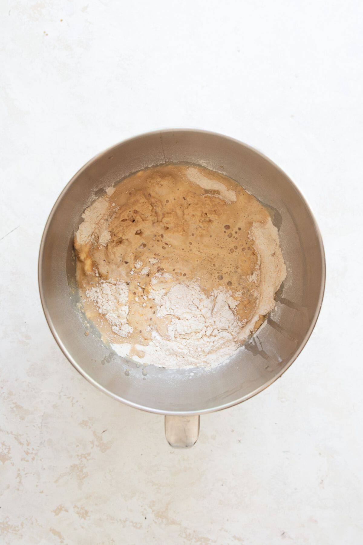 Yeasted almond milk being poured over flour and salt in a stand mixer bowl.