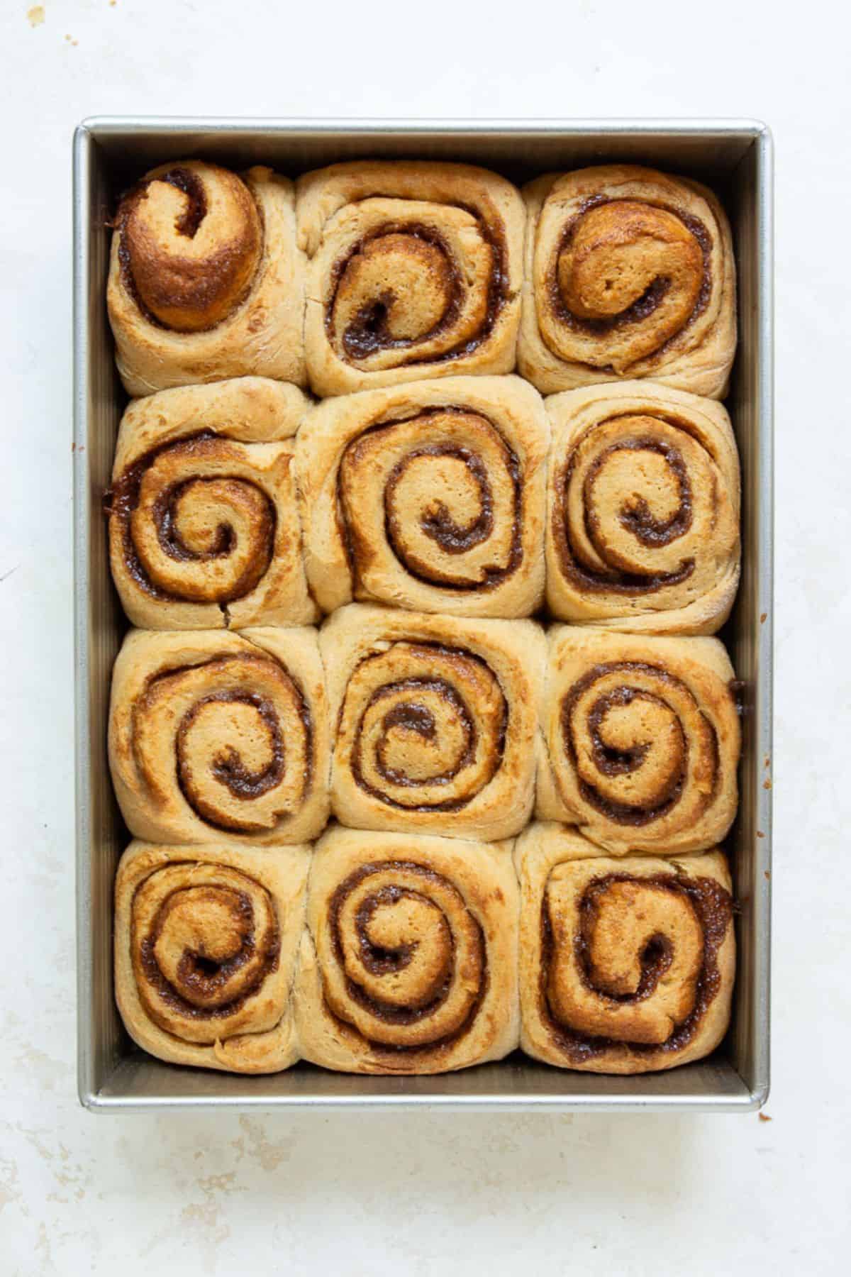 Twelve golden brown healthy cinnamon rolls in a baking pan, freshly out of the oven.
