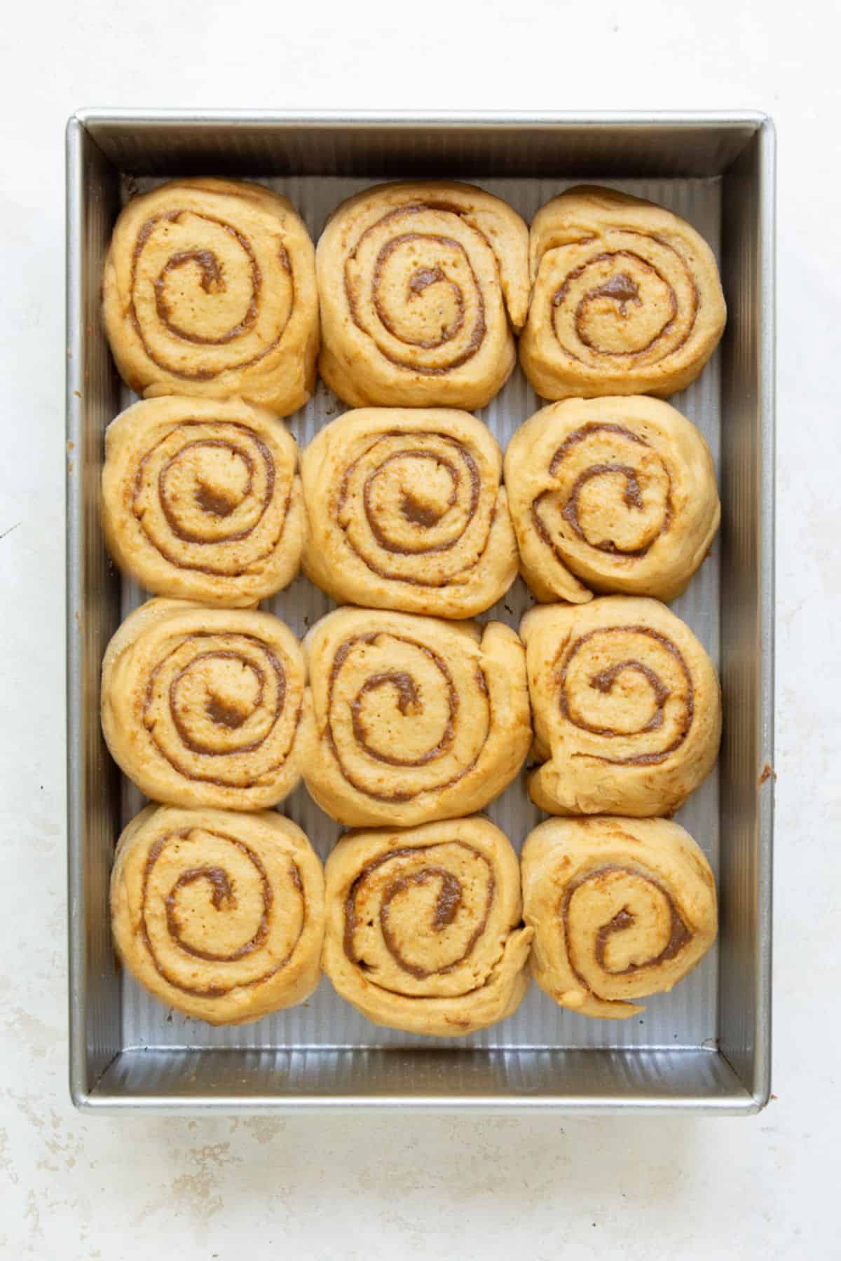 Twelve unbaked cinnamon rolls arranged in a baking pan after their second rise.