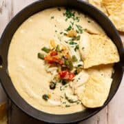 Creamy high protein cottage cheese queso dip in a cast iron skillet topped with cilantro, poblano, and onions, served with tortilla chips.