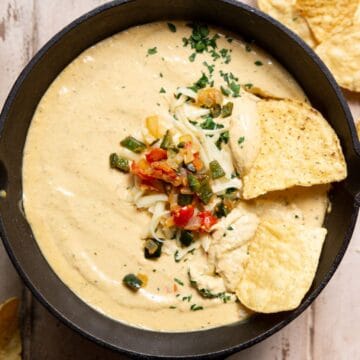 Creamy high protein cottage cheese queso dip in a cast iron skillet topped with cilantro, poblano, and onions, served with tortilla chips.
