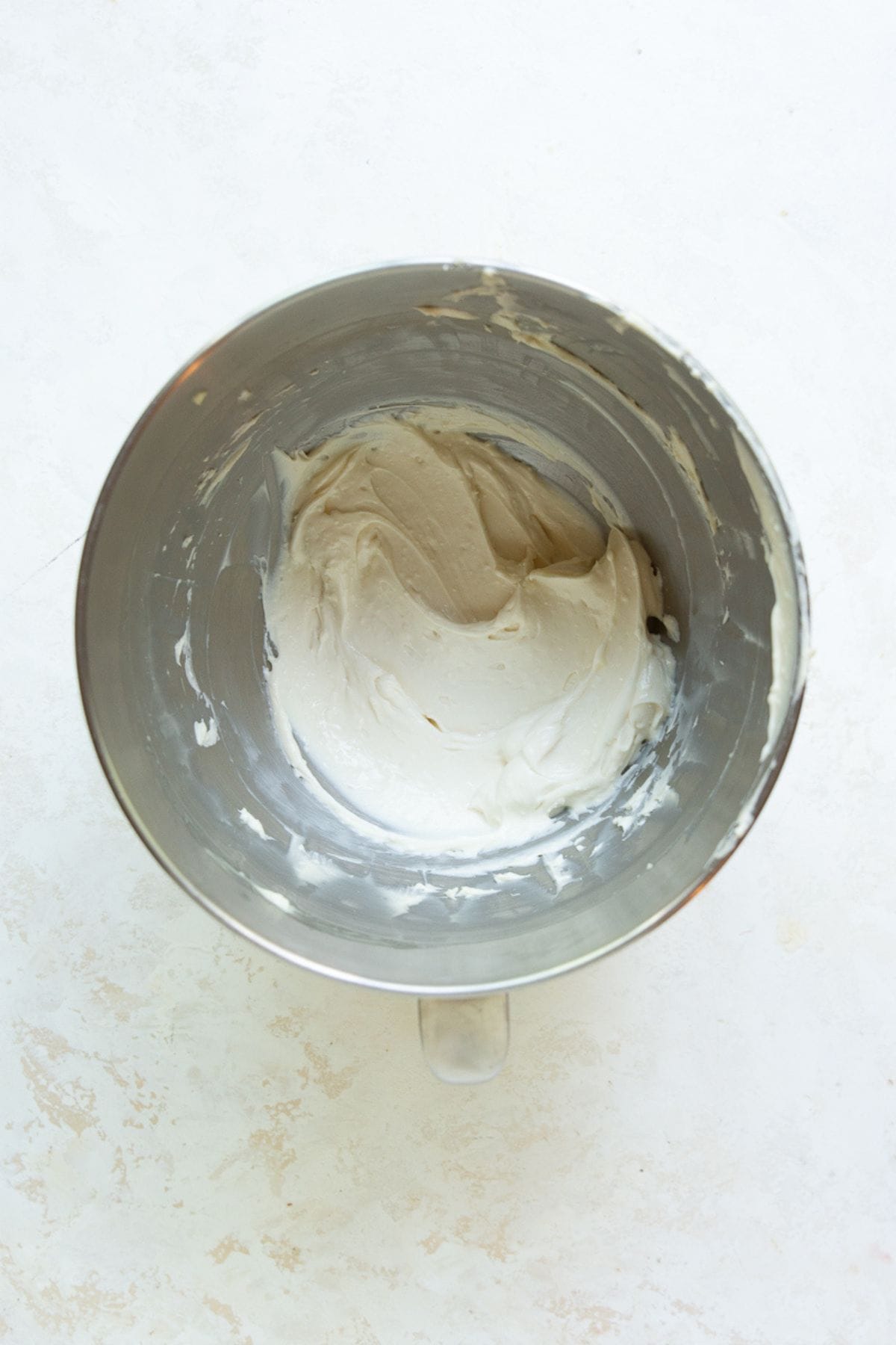 Greek yogurt and cream cheese icing whipped to a smooth, fluffy consistency in a metal mixing bowl.