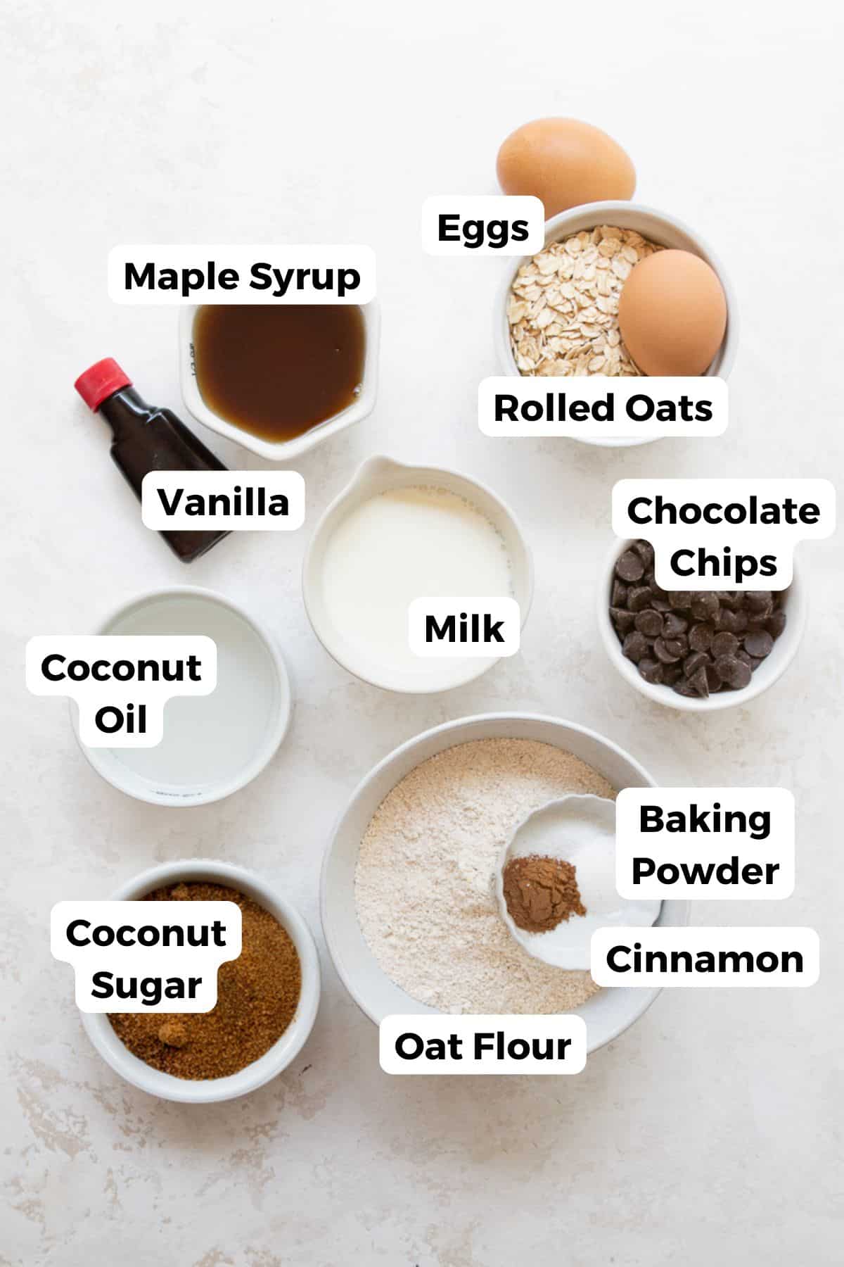 Labeled ingredients for healthy chocolate chip oatmeal bars: rolled oats, oat flour, eggs, milk, maple syrup, coconut oil, coconut sugar, vanilla, cinnamon, baking powder, and chocolate chips.