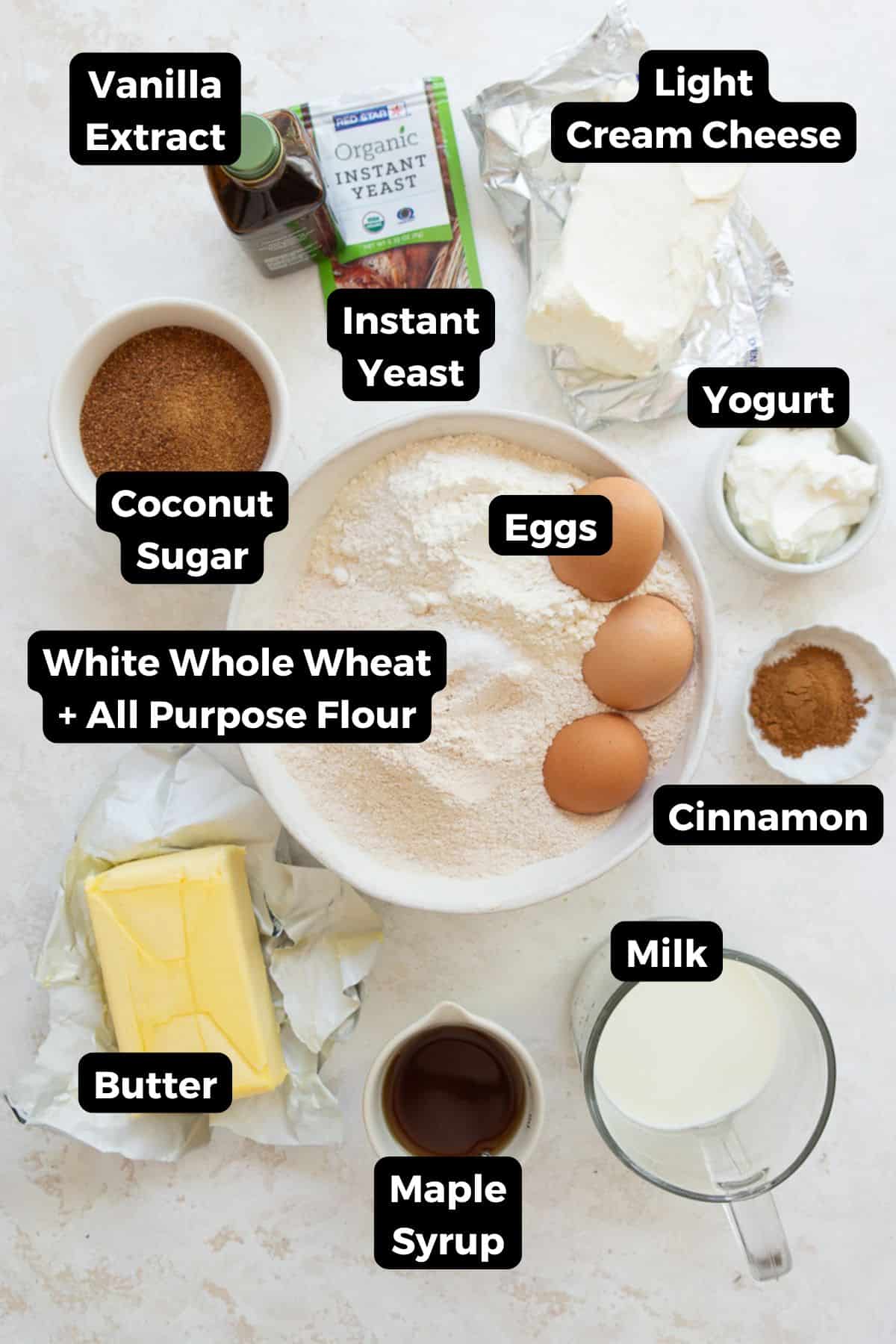 All ingredients for healthy cinnamon rolls with Greek yogurt icing measured into bowls, including white whole wheat flour, all-purpose flour, coconut sugar, butter, eggs, almond milk, Greek yogurt, cream cheese, and maple syrup.