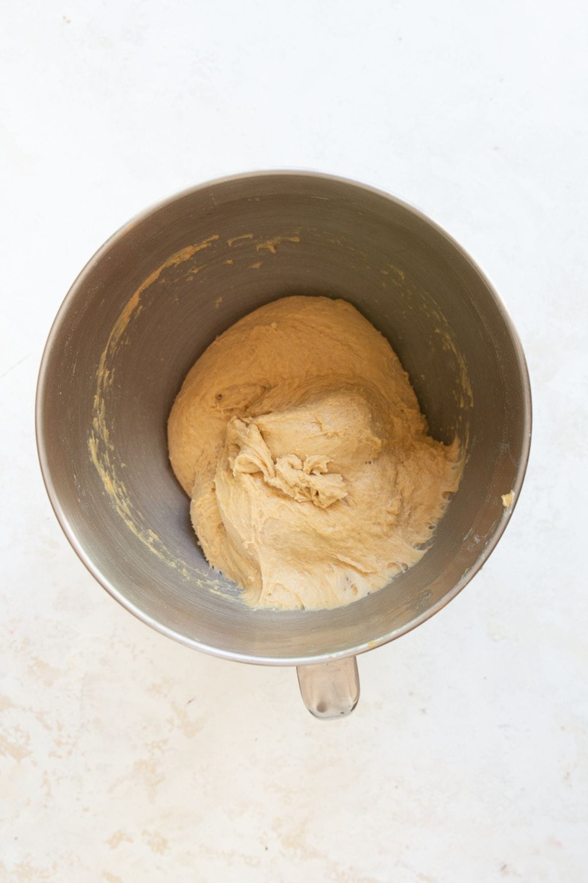 Cinnamon roll dough being kneaded with a dough hook attachment in a stand mixer.