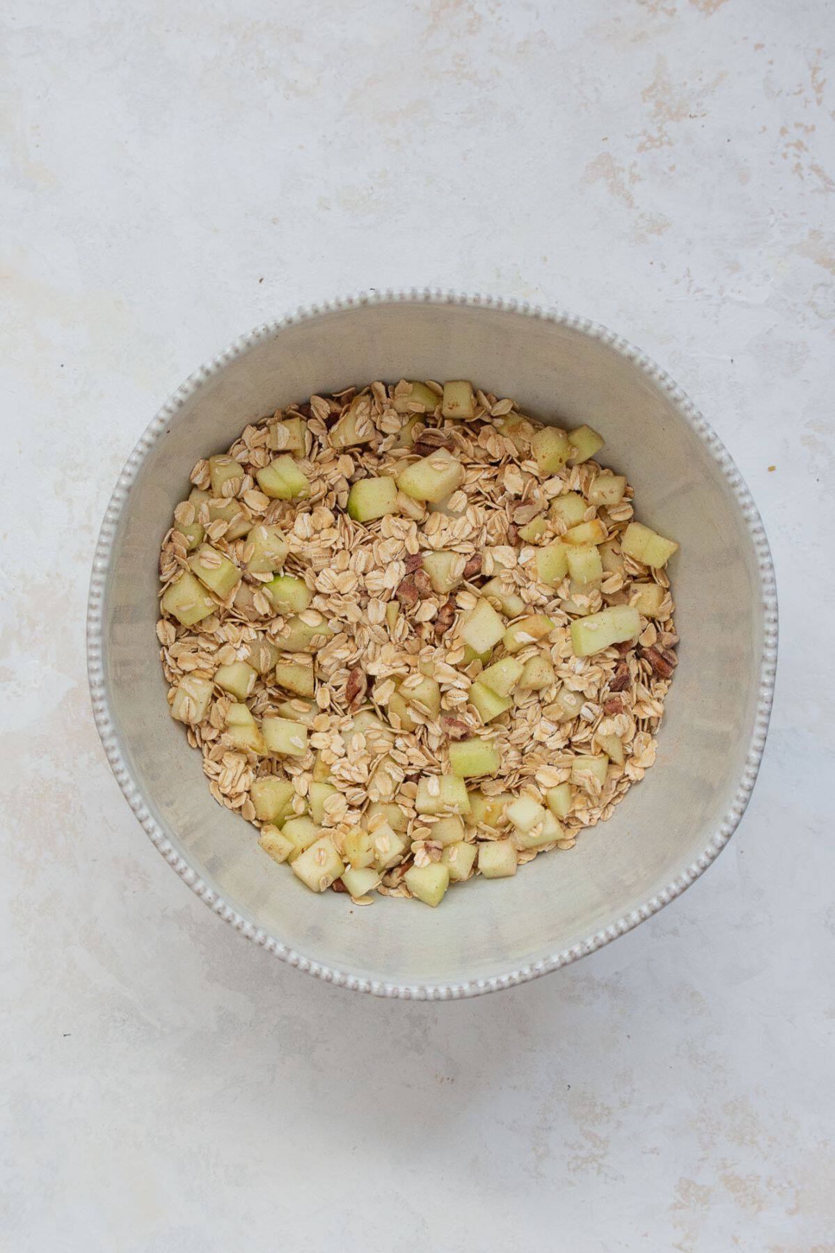 Rolled oats, chopped apples, and pecans tossed together in a mixing bowl.