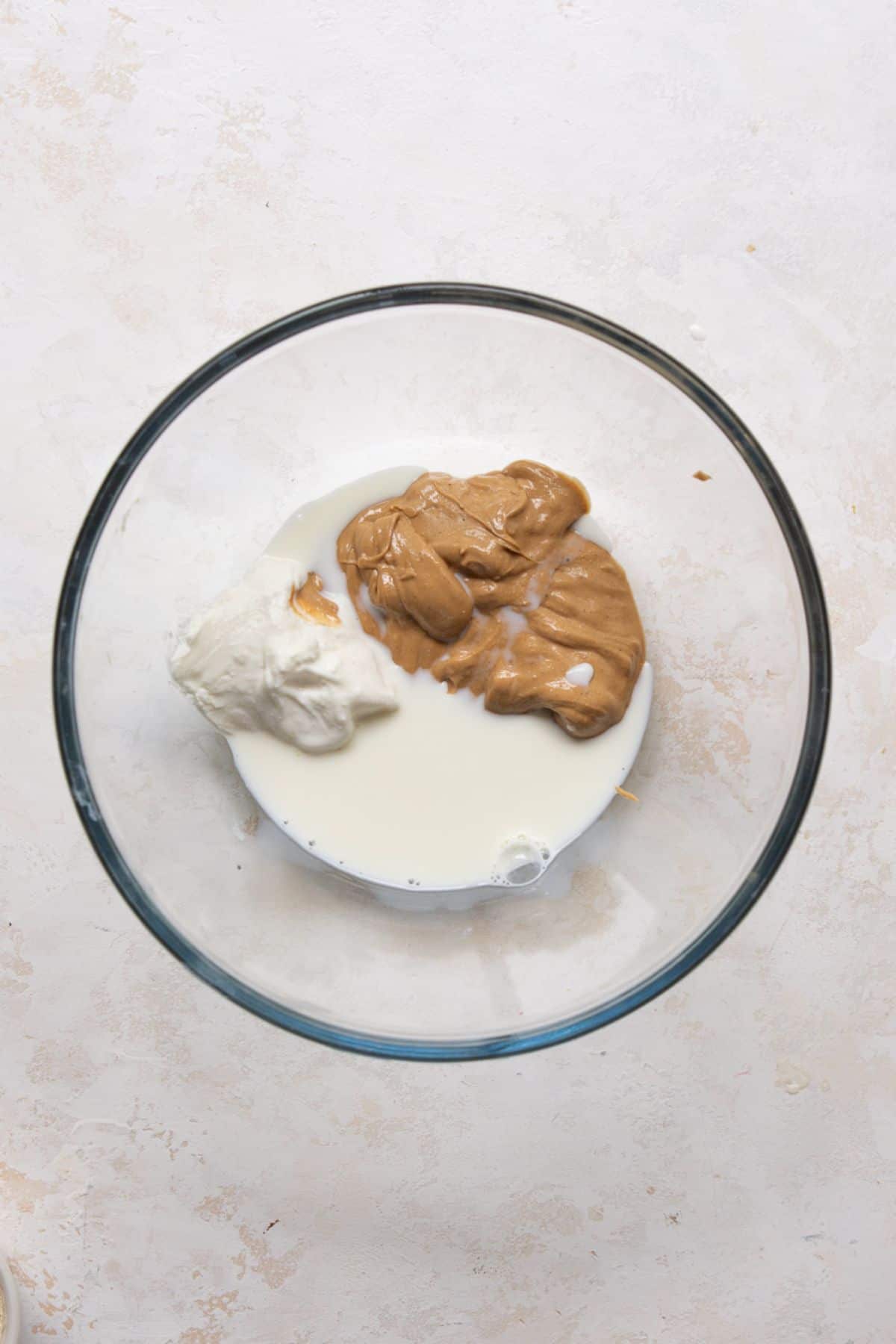 Almond butter, blended cottage cheese, milk, and maple syrup in a glass mixing bowl before whisking.