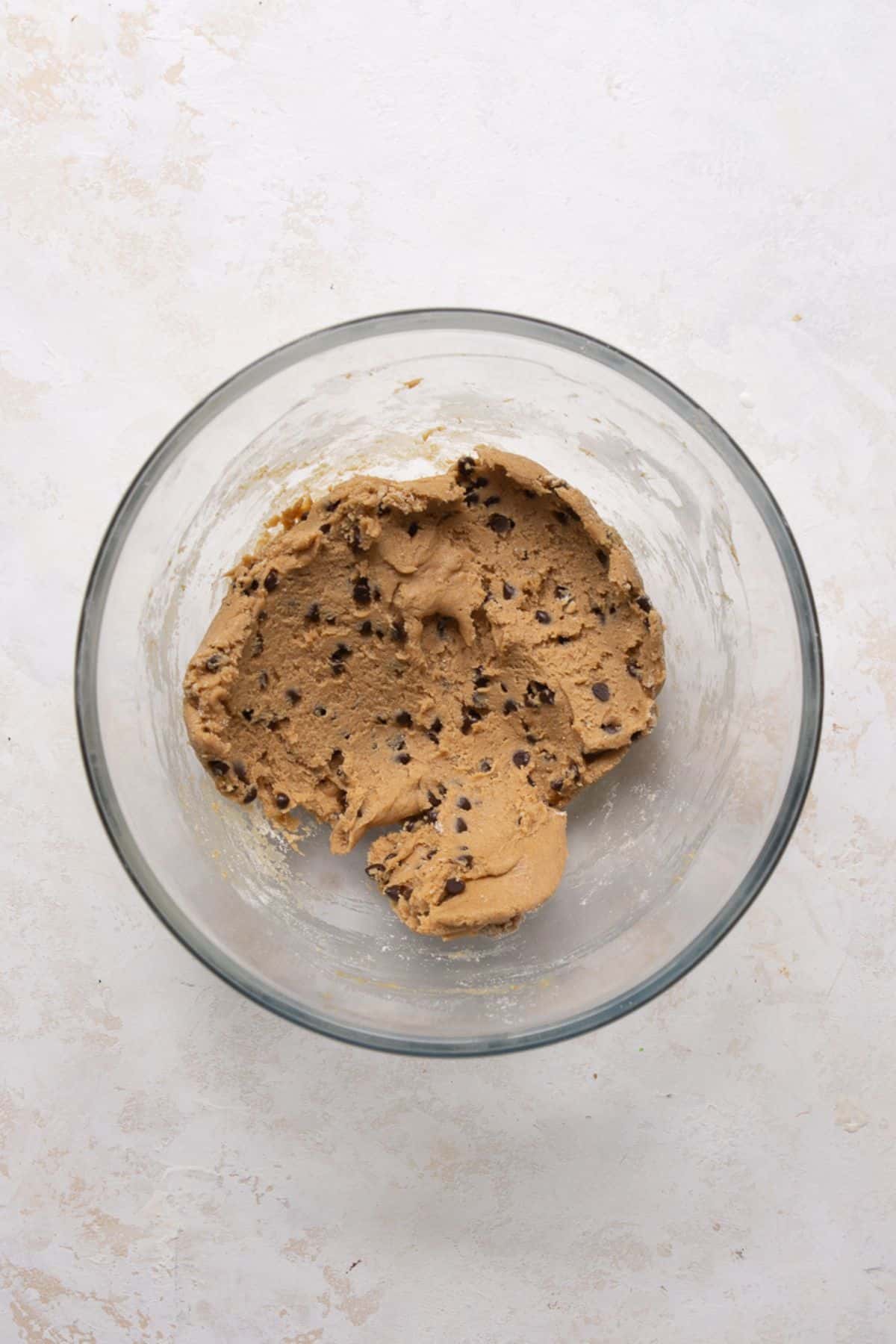 Finished high-protein edible cookie dough with mini chocolate chips folded in, in a glass mixing bowl.