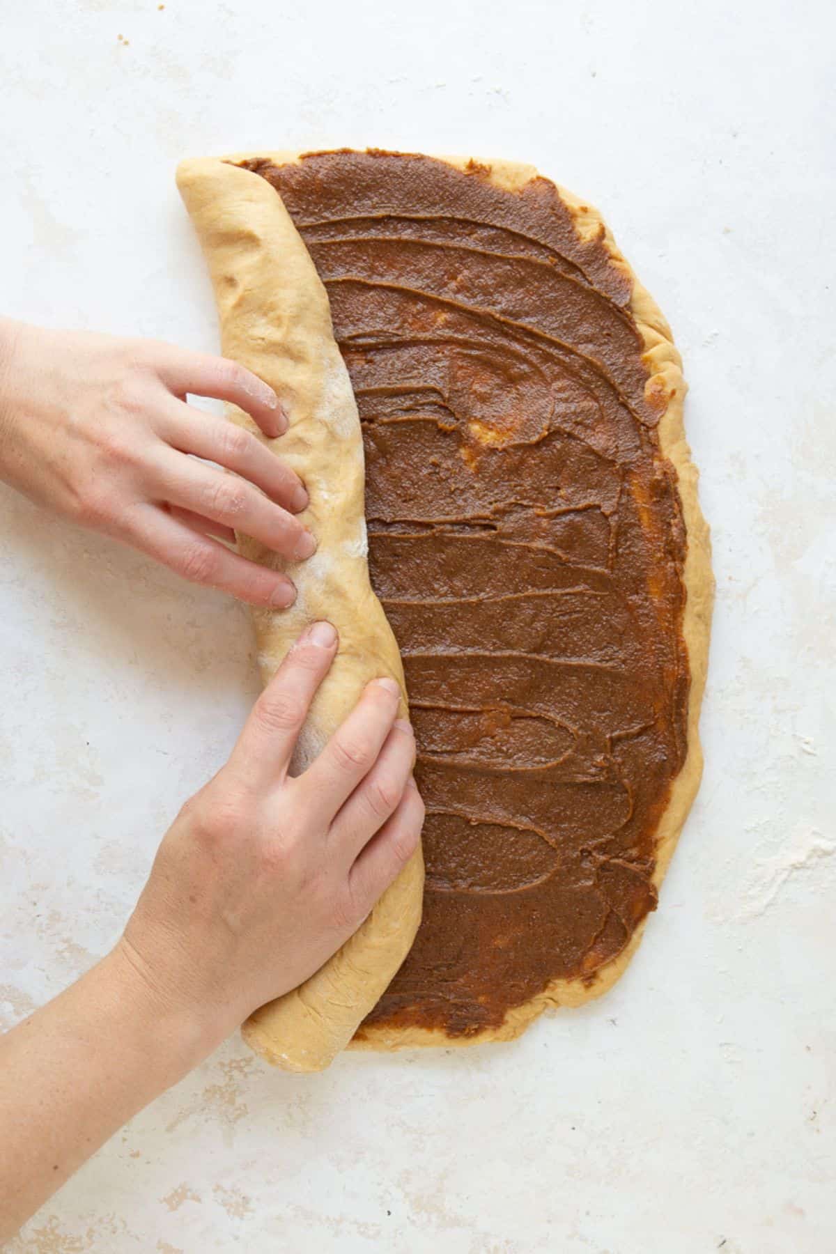 Hands rolling cinnamon-filled dough into a tight log.