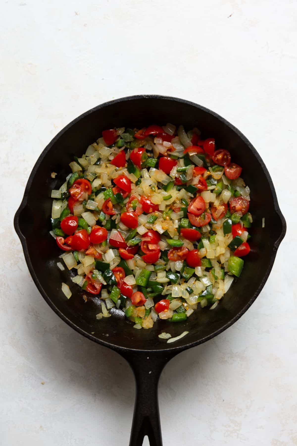 Sautéed poblano, onion, and chopped tomato cooking together in a cast iron pan.