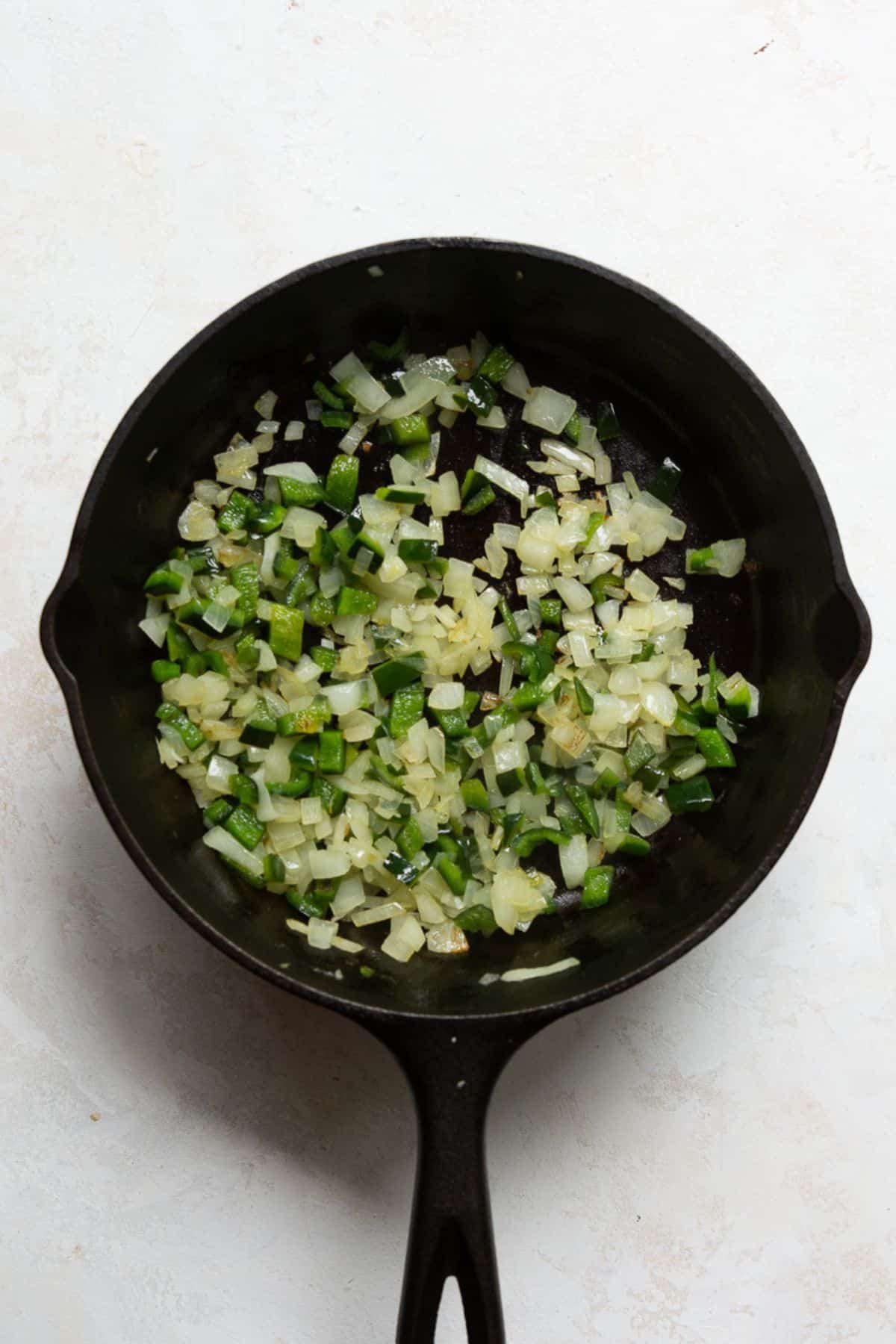 Diced poblano peppers and white onion sautéing in a cast iron skillet.