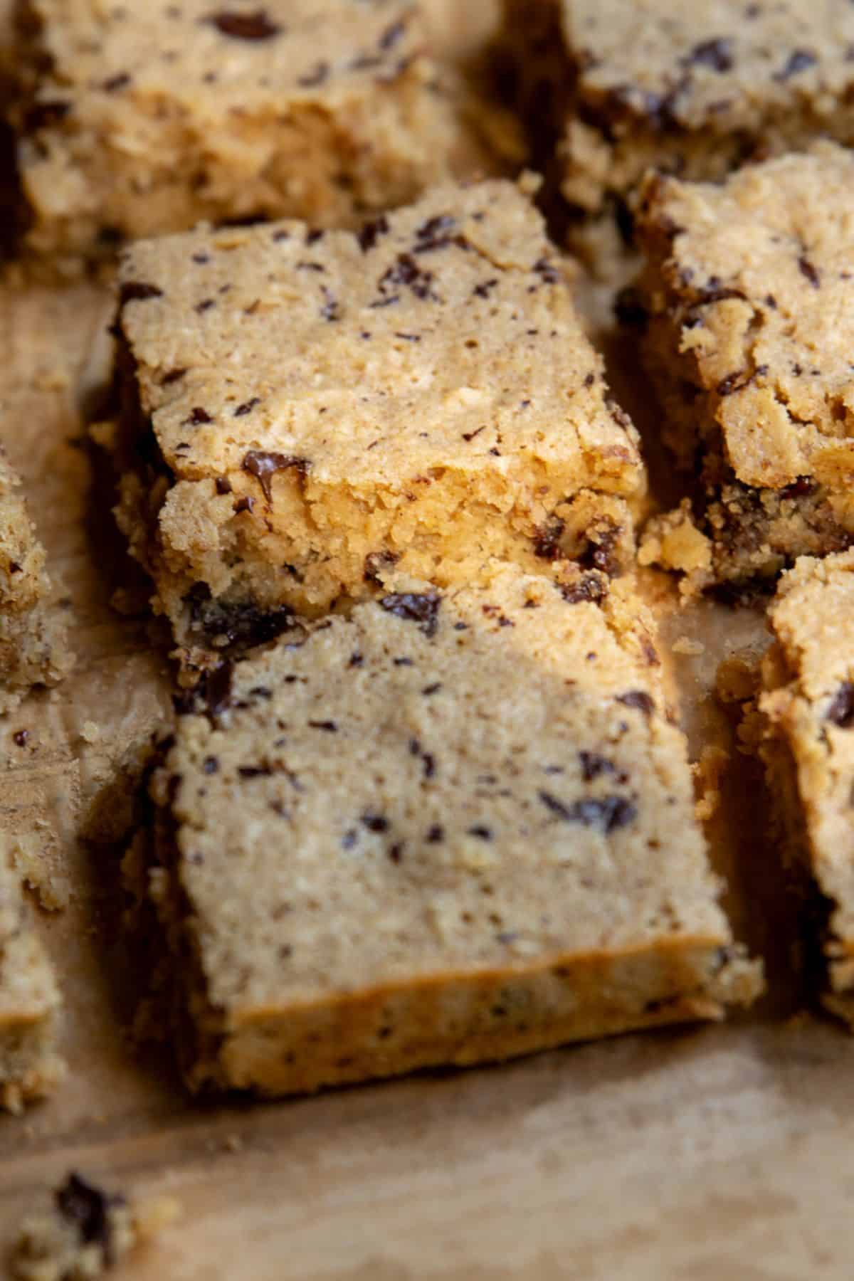 Sliced healthy chocolate chip oatmeal bars on parchment paper, cut into 12 squares with melted dark chocolate on top.