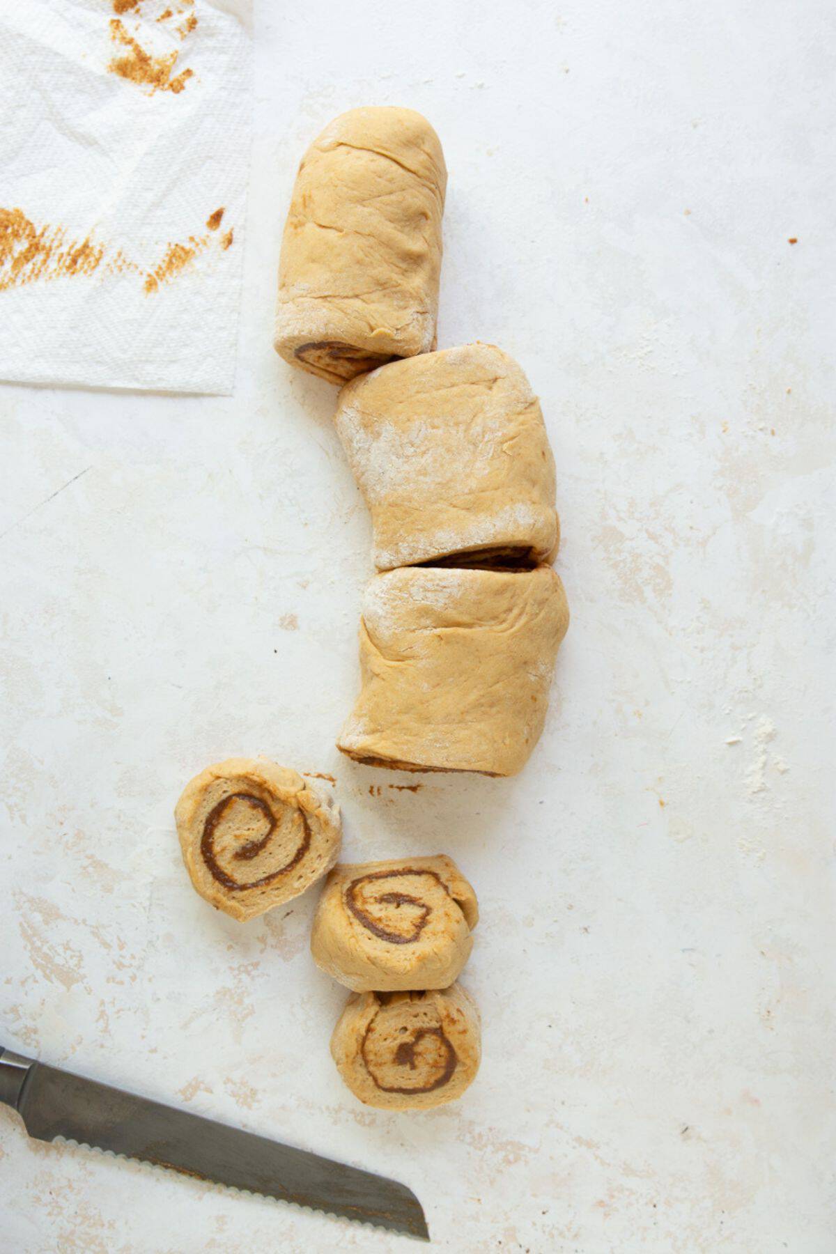 Healthy cinnamon roll dough log being sliced into 12 even rolls with a serrated knife.