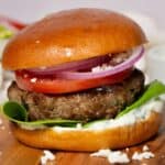 Greek bison burger with feta, tzatziki, tomato, and red onion on a brioche bun.