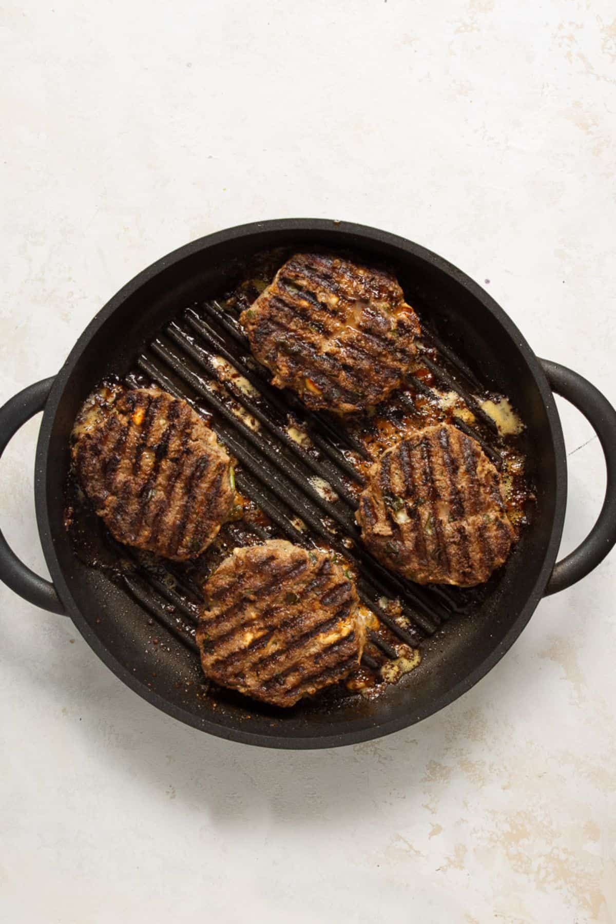 Bison burgers with grill marks searing on a cast iron grill skillet.