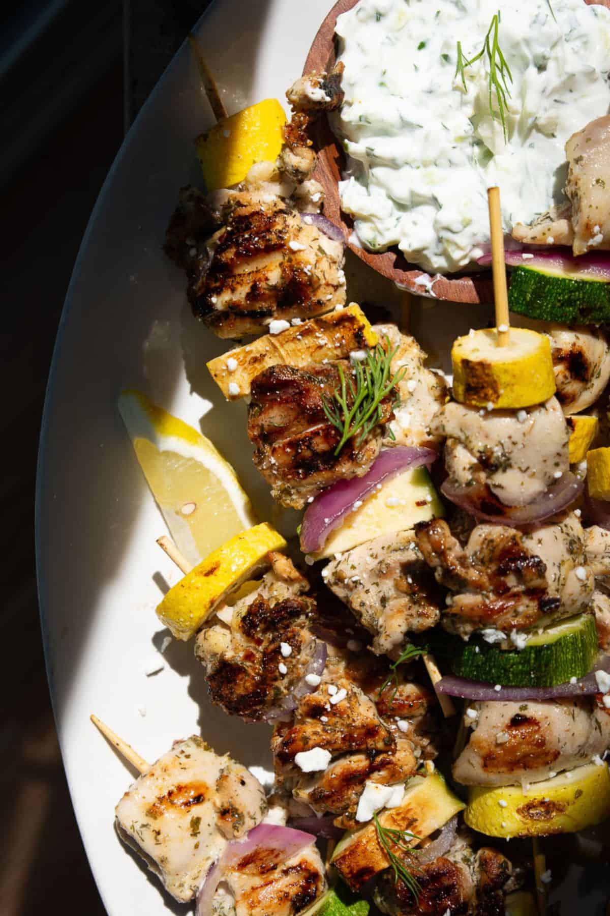 Close-up of charred lemony Greek chicken kabobs topped with crumbled feta and fresh dill.