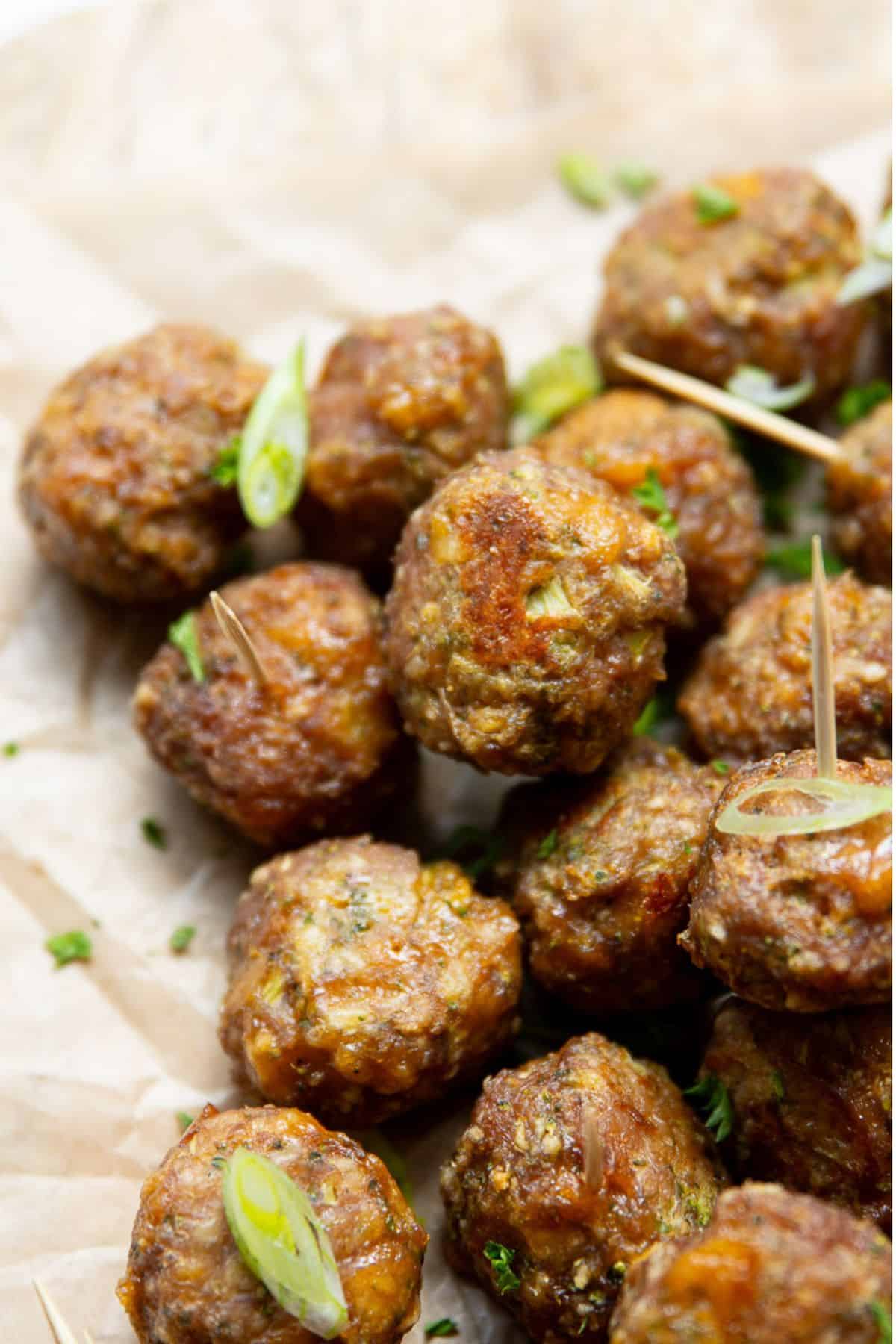 Close up healthy broccoli cheddar turkey meatballs with crispy golden edges, garnished with scallions and parsley on parchment paper.