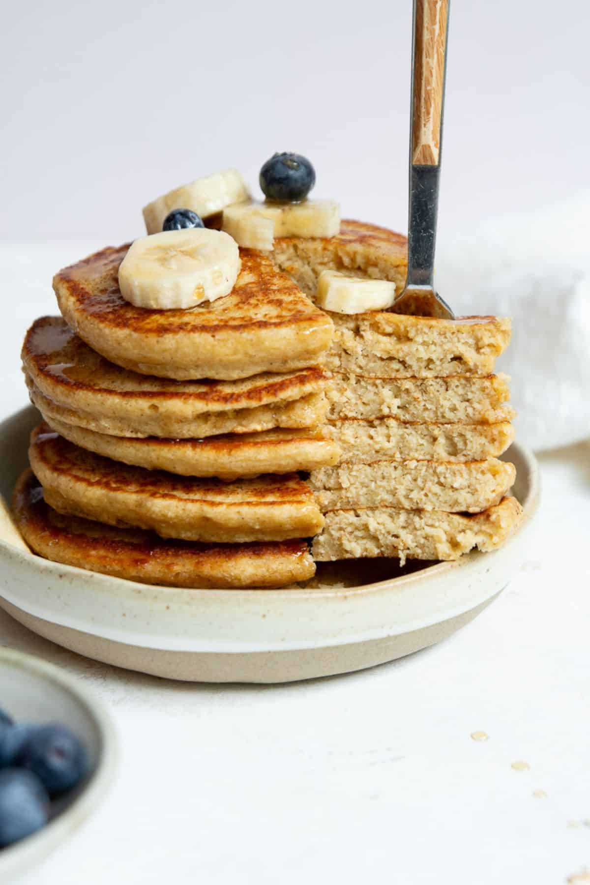 Fork lifting a slice from a stack of protein oatmeal pancakes showing the fluffy inside.