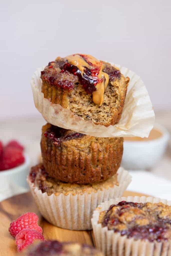 Stack of healthy peanut butter and jelly banana muffins with a bite taken from the top muffin showing the soft almond flour crumb.