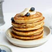 Stack of fluffy and healthy protein oatmeal blender pancakes topped with banana slices and blueberries.