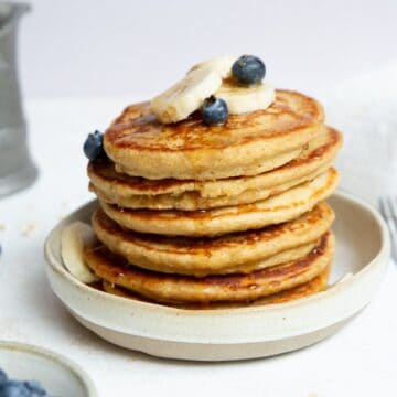 Stack of fluffy and healthy protein oatmeal blender pancakes topped with banana slices and blueberries.
