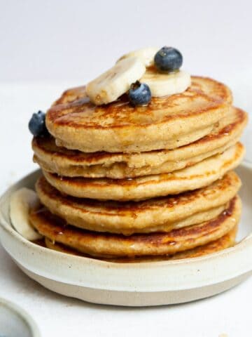 Stack of fluffy and healthy protein oatmeal blender pancakes topped with banana slices and blueberries.