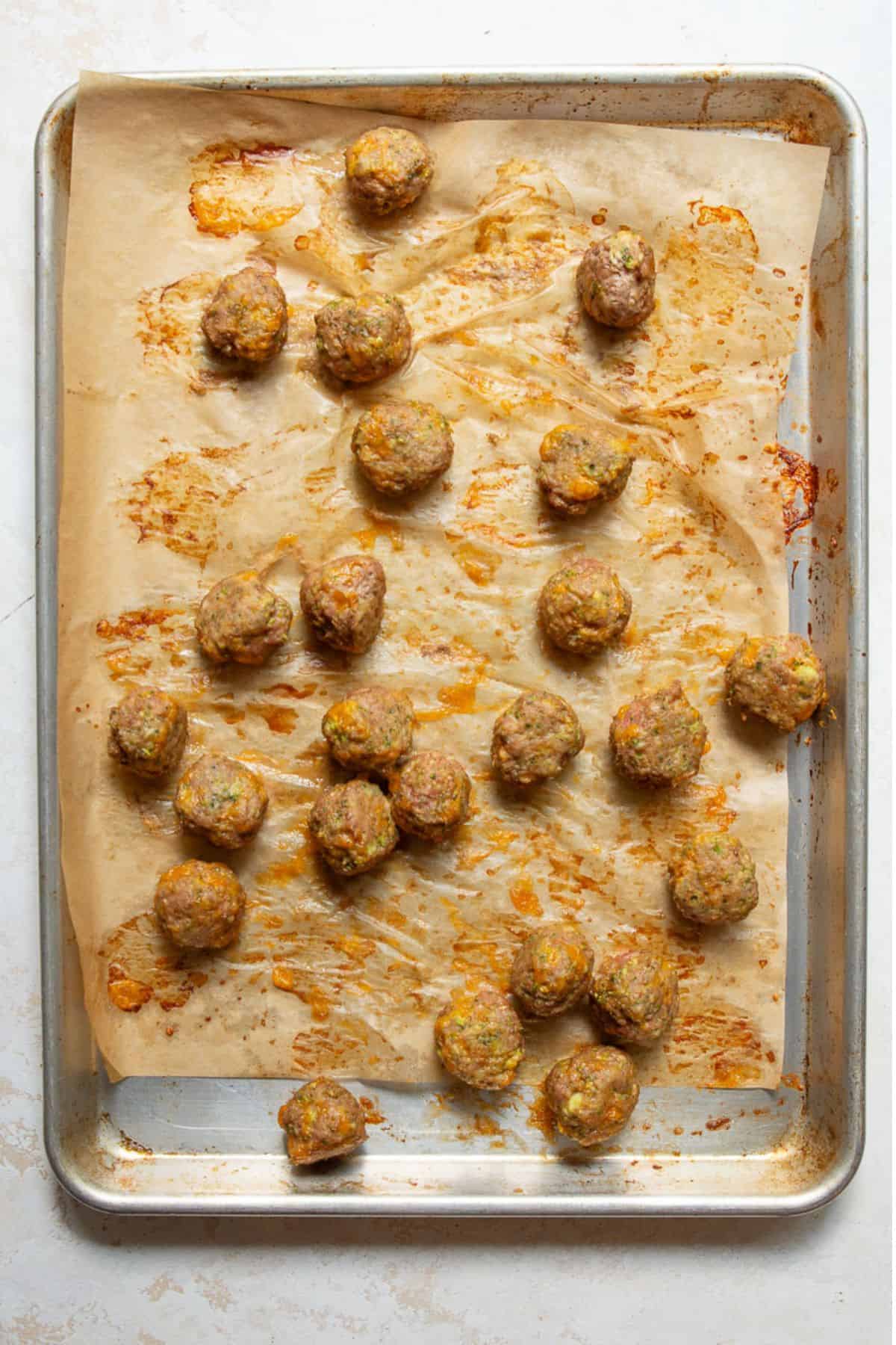 Golden baked broccoli cheddar turkey meatballs on a parchment-lined baking sheet fresh from the oven.