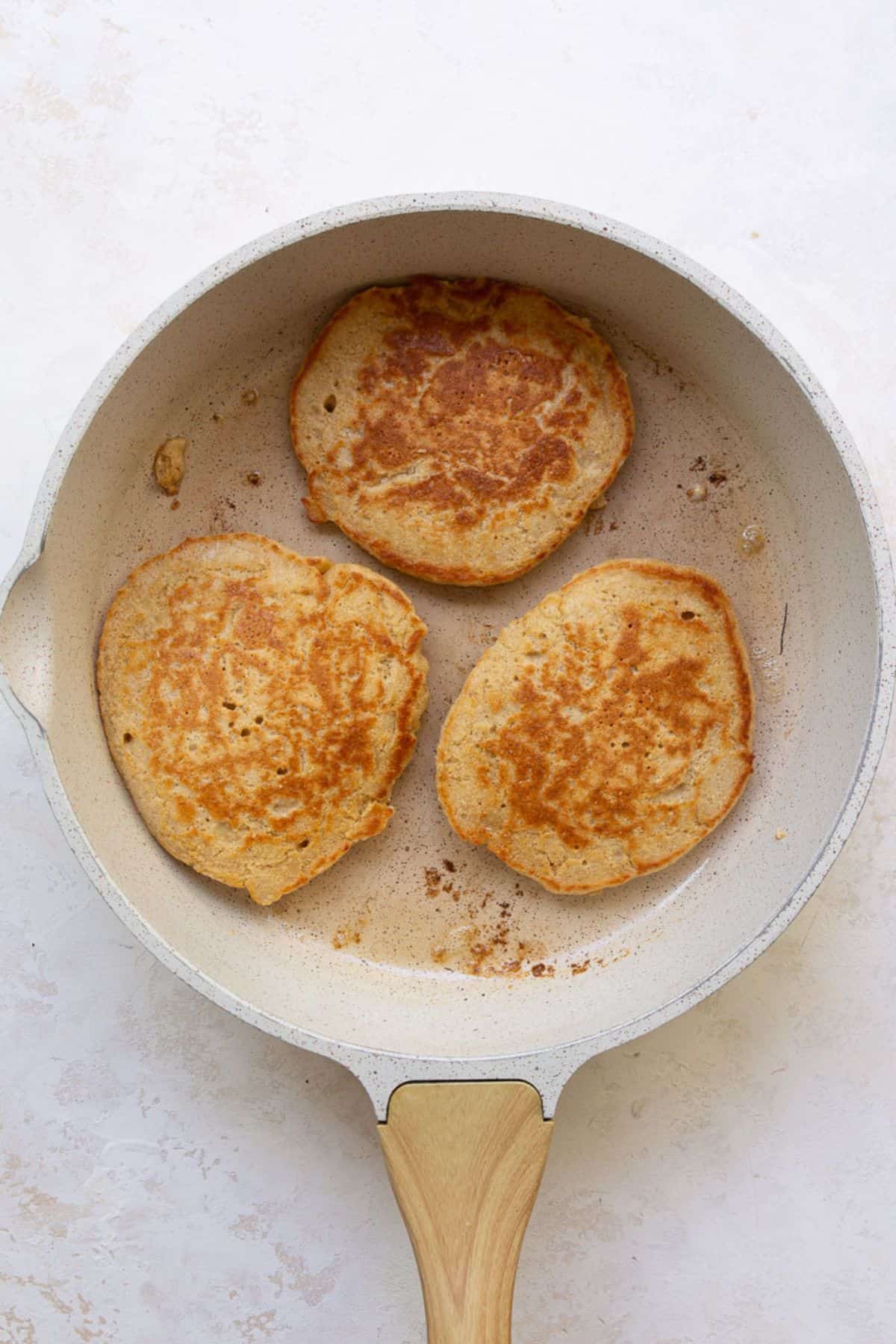Golden brown protein oatmeal pancakes flipped in a pan.