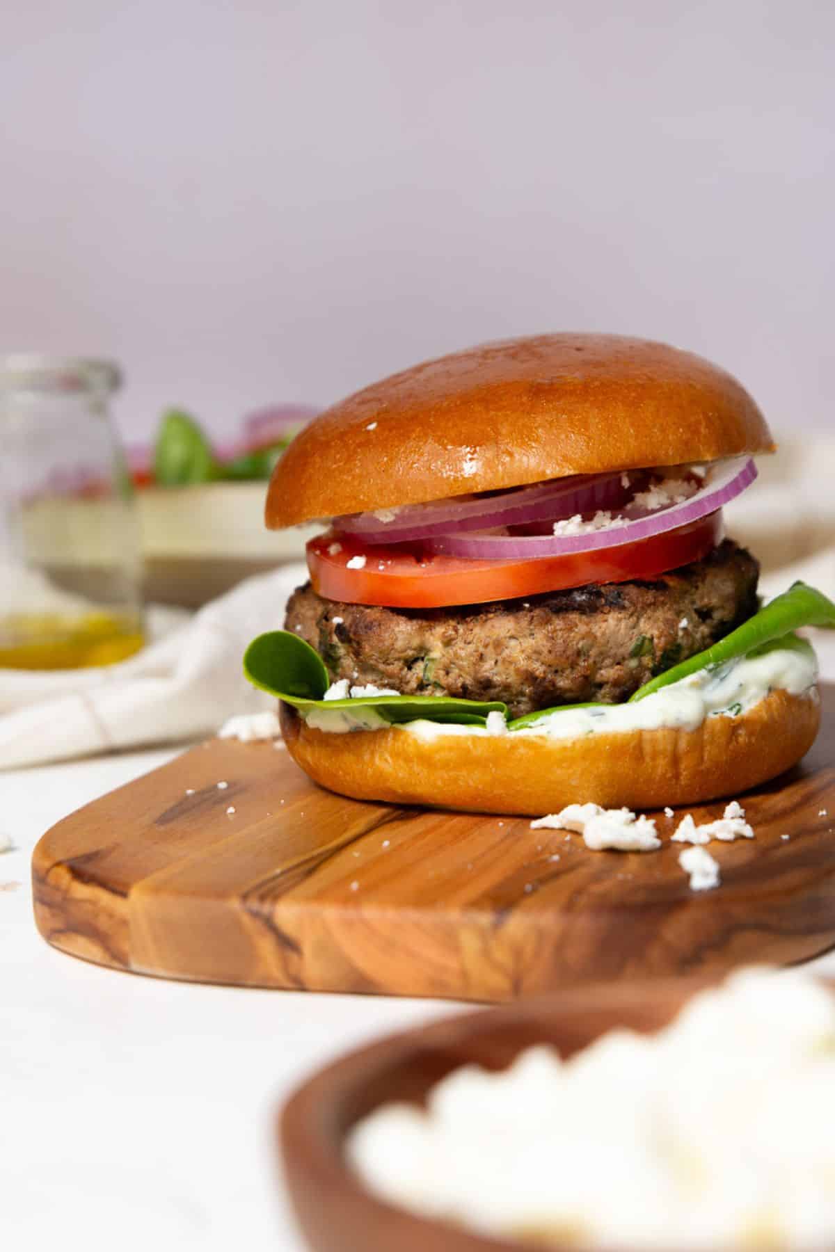 Greek bison burger with feta, tzatziki, tomato, and red onion on a brioche bun.