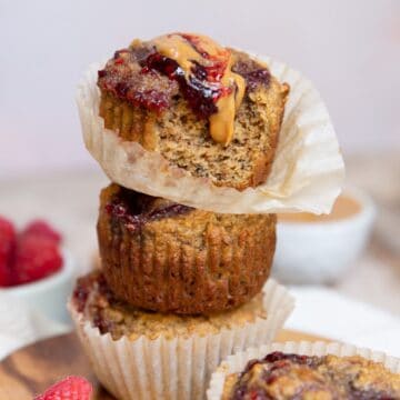 Healthy peanut butter and jelly banana muffins stacked with peanut butter and raspberry jam swirled over the top.
